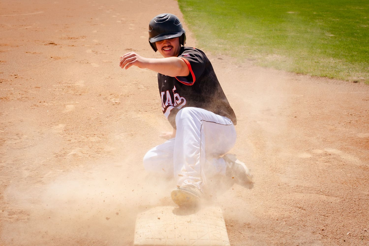 Baseball player sliding into base creating dust cloud during game action.