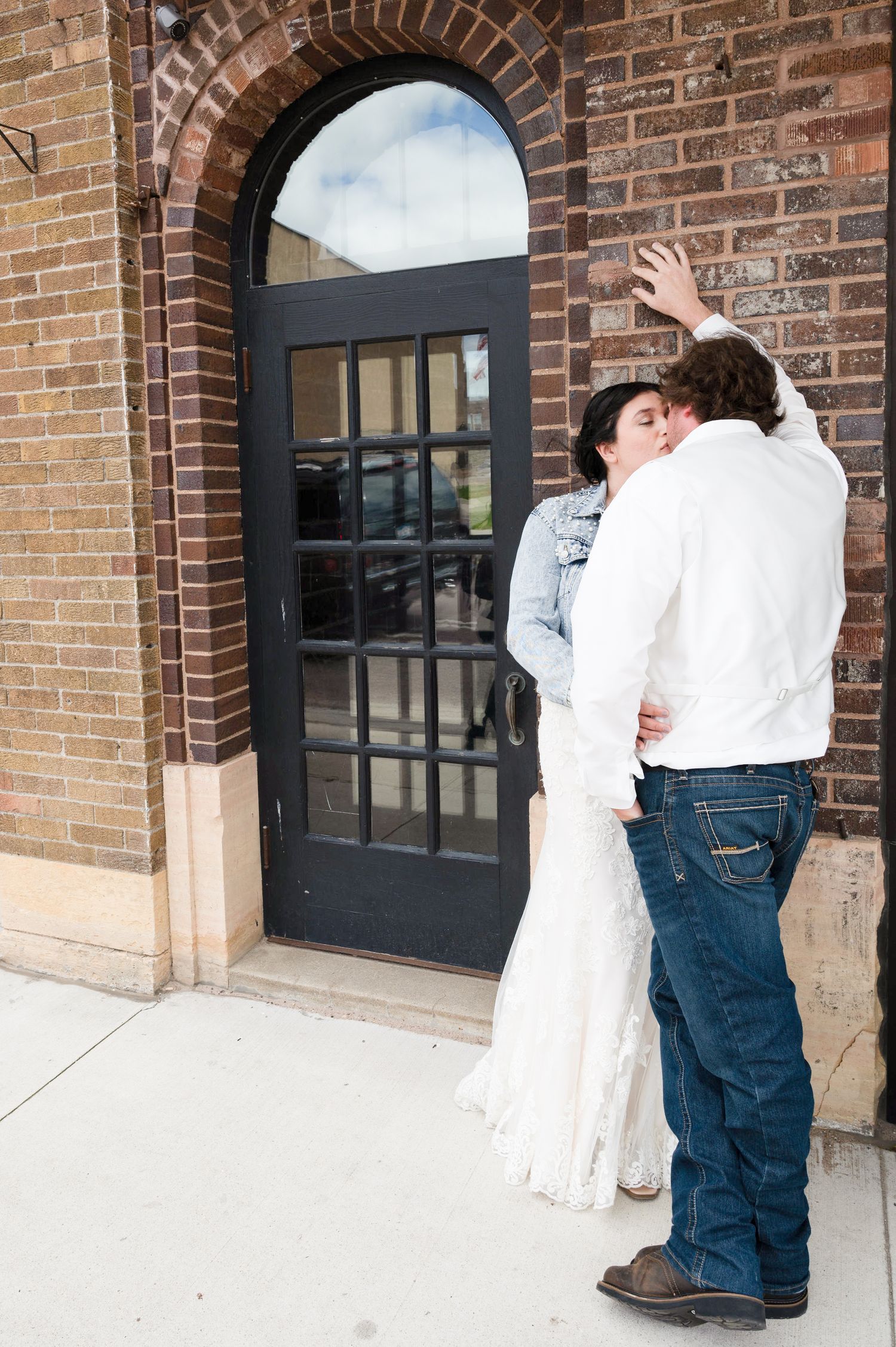 A romantic moment shared between newlyweds by a brick archway and black door.