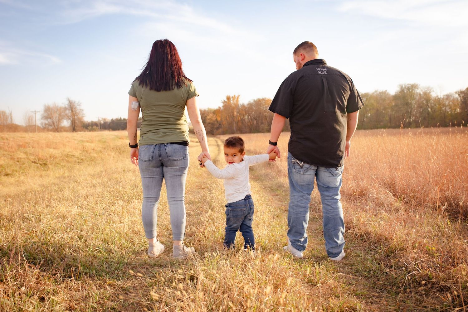 Family enjoying a stroll together on a path through tall golden grass.
