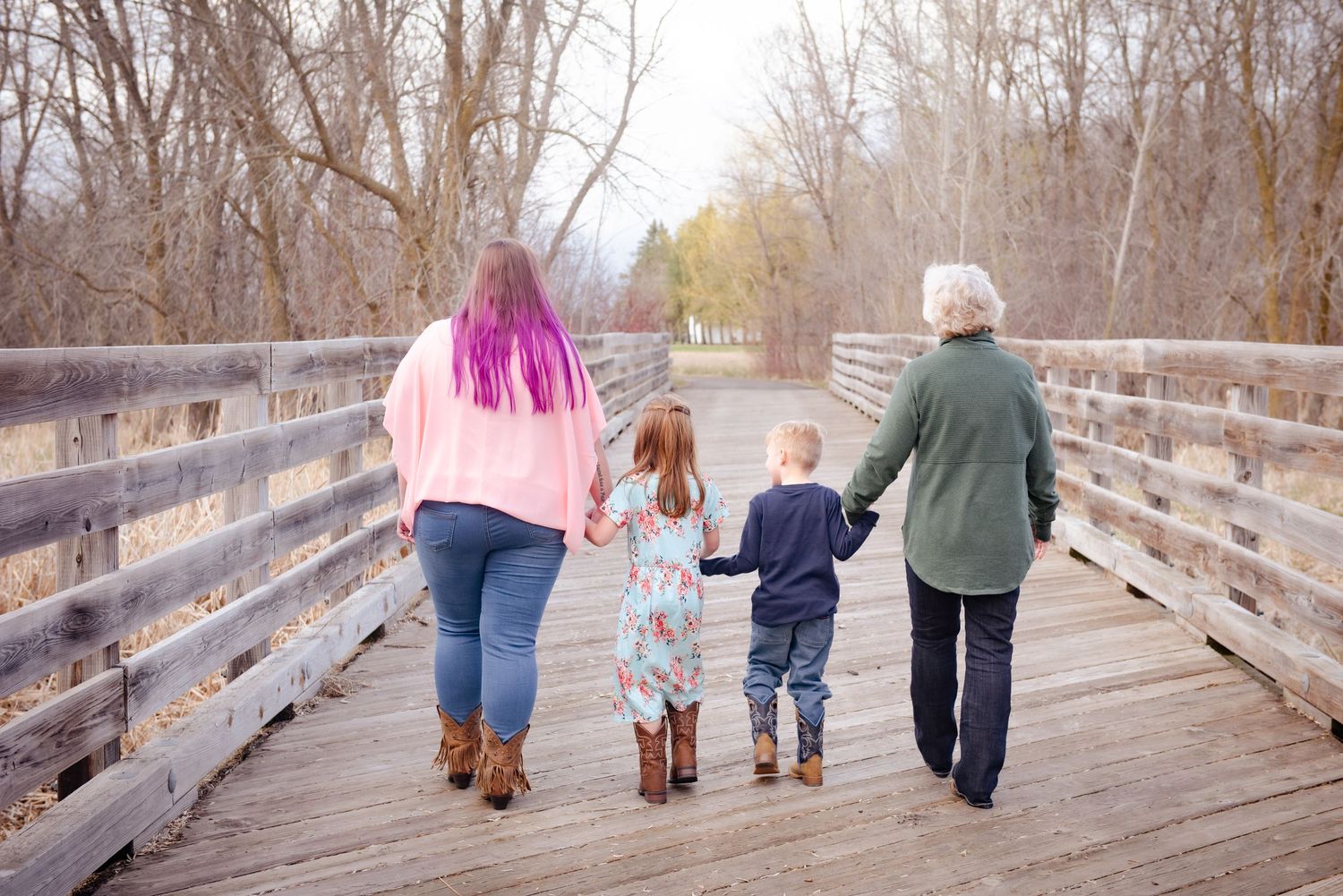 Four people walking hand in hand away from camera on wooden bridge walkway.