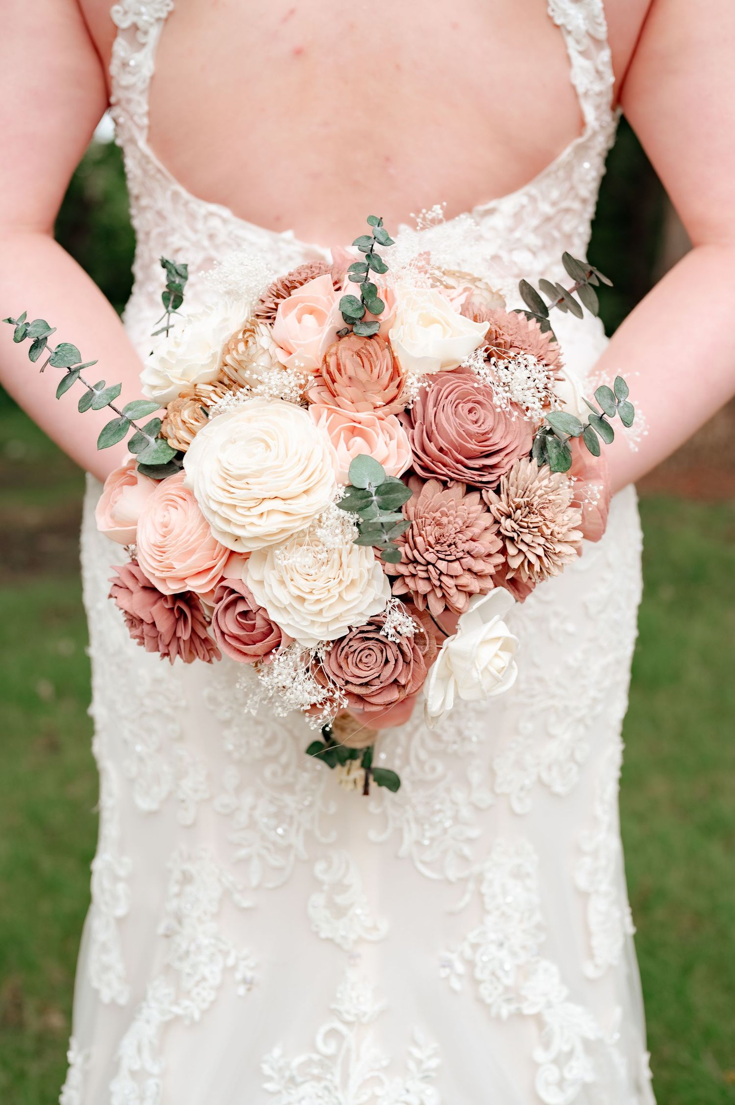 Elegant bridal bouquet with dusty rose and white flowers held against lace wedding dress.