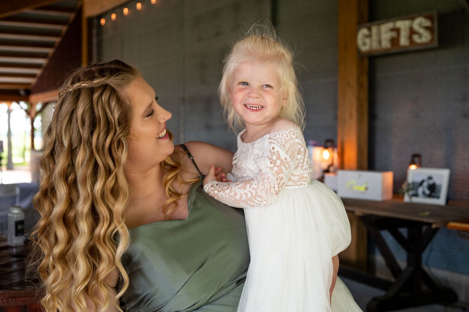 Joyful moment shared between attendee and young flower girl in white lace dress.