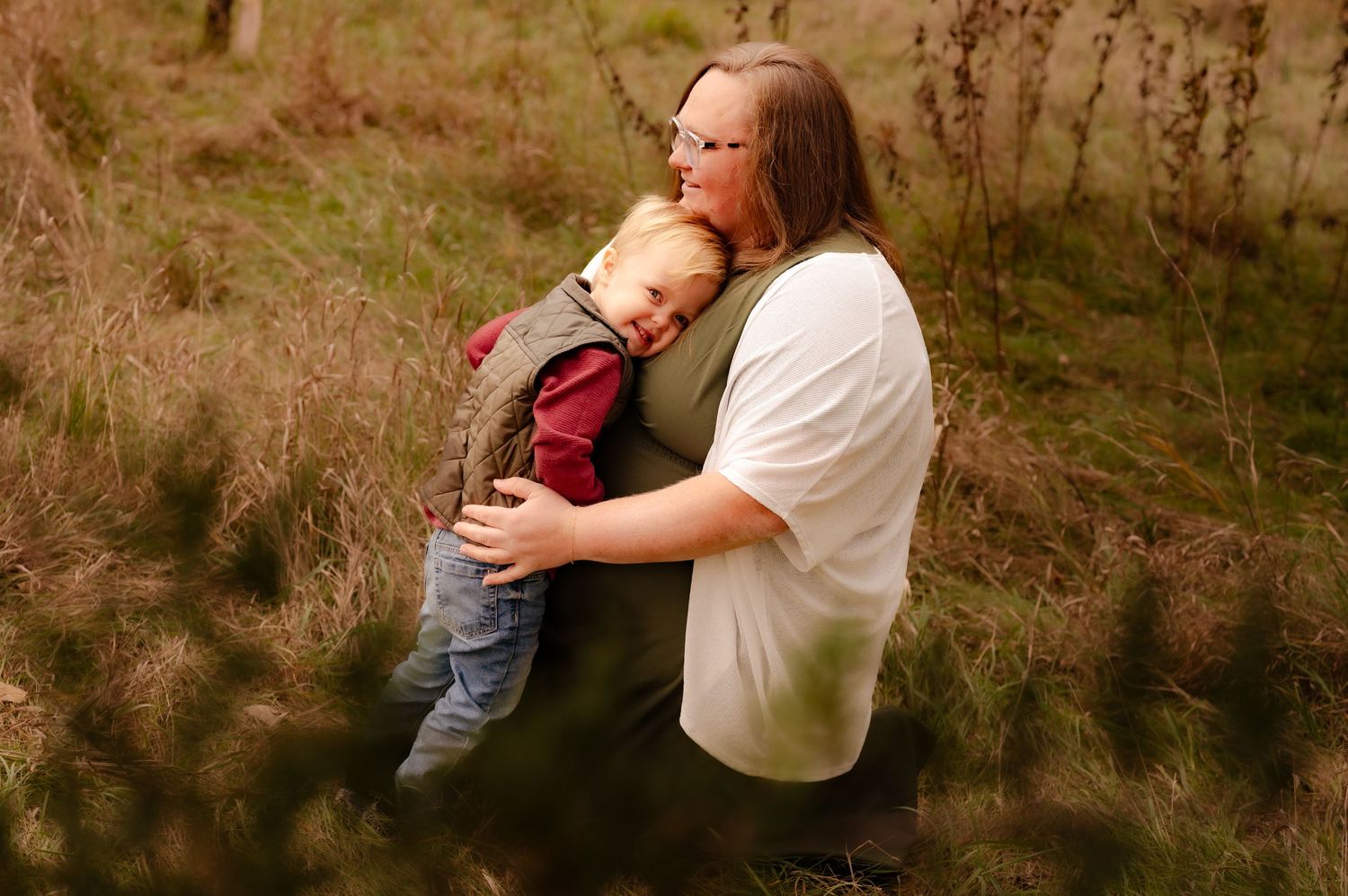 A tender moment captured in nature as parent and baby embrace in a sunlit field with tall grass.
