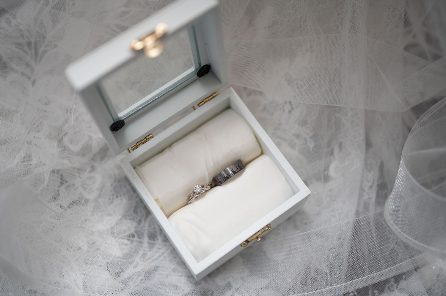 White decorative box containing wedding rings on delicate tulle fabric.