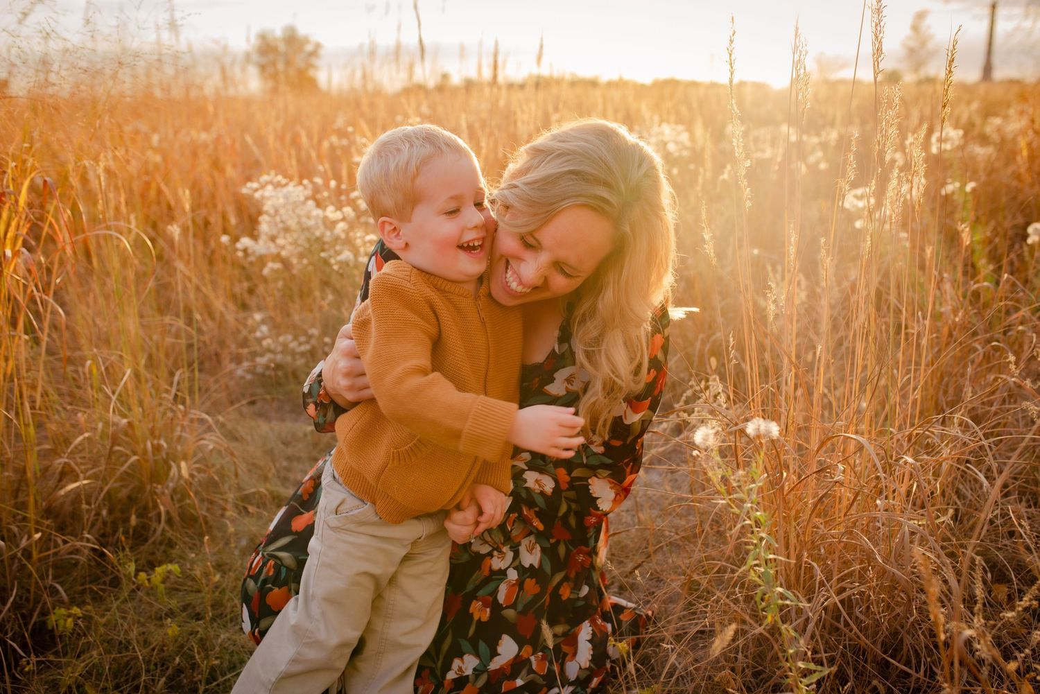 Intimate family moment captured in golden sunlit field with tall grass.