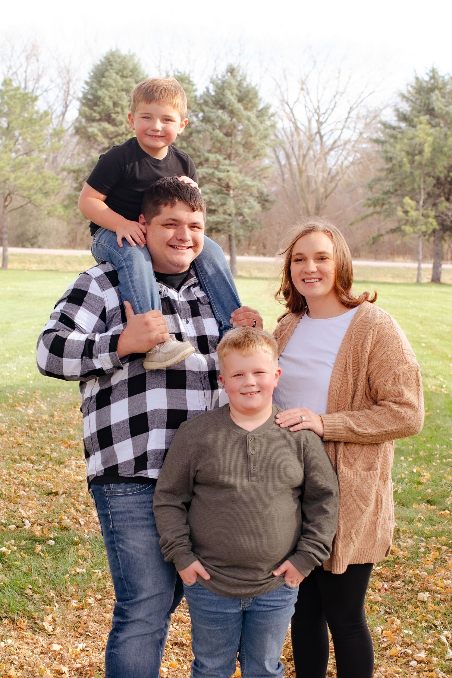 A happy family of four posing together outdoors on an autumn day with fallen leaves.