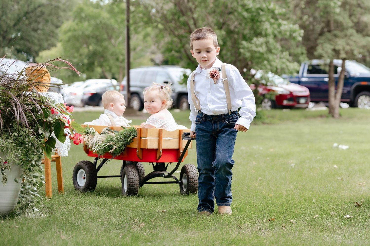 Children ride in a red wagon at an outdoor wedding event.