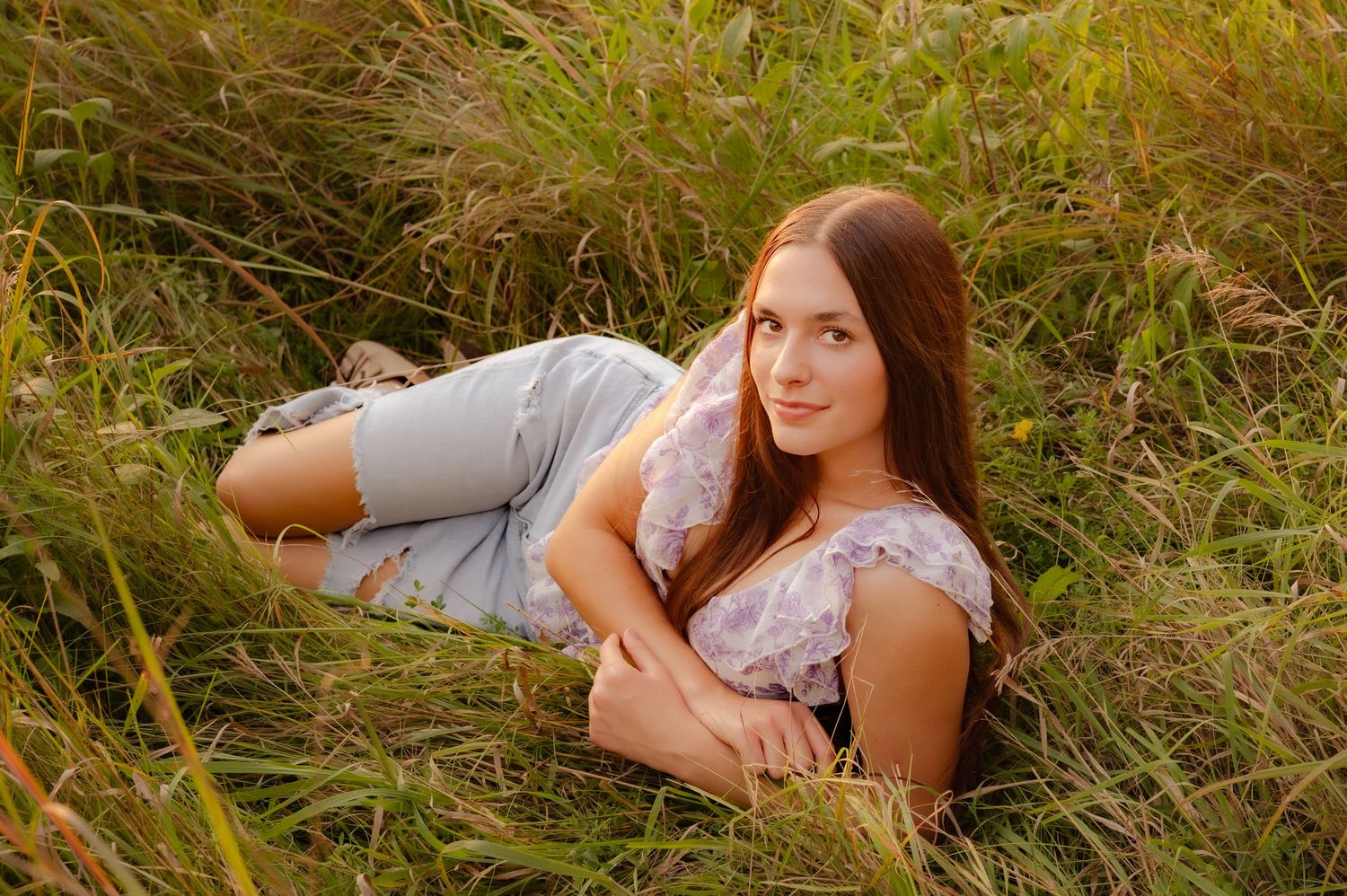 Portrait series in a golden meadow with someone wearing a floral dress lying in tall grass during sunset.