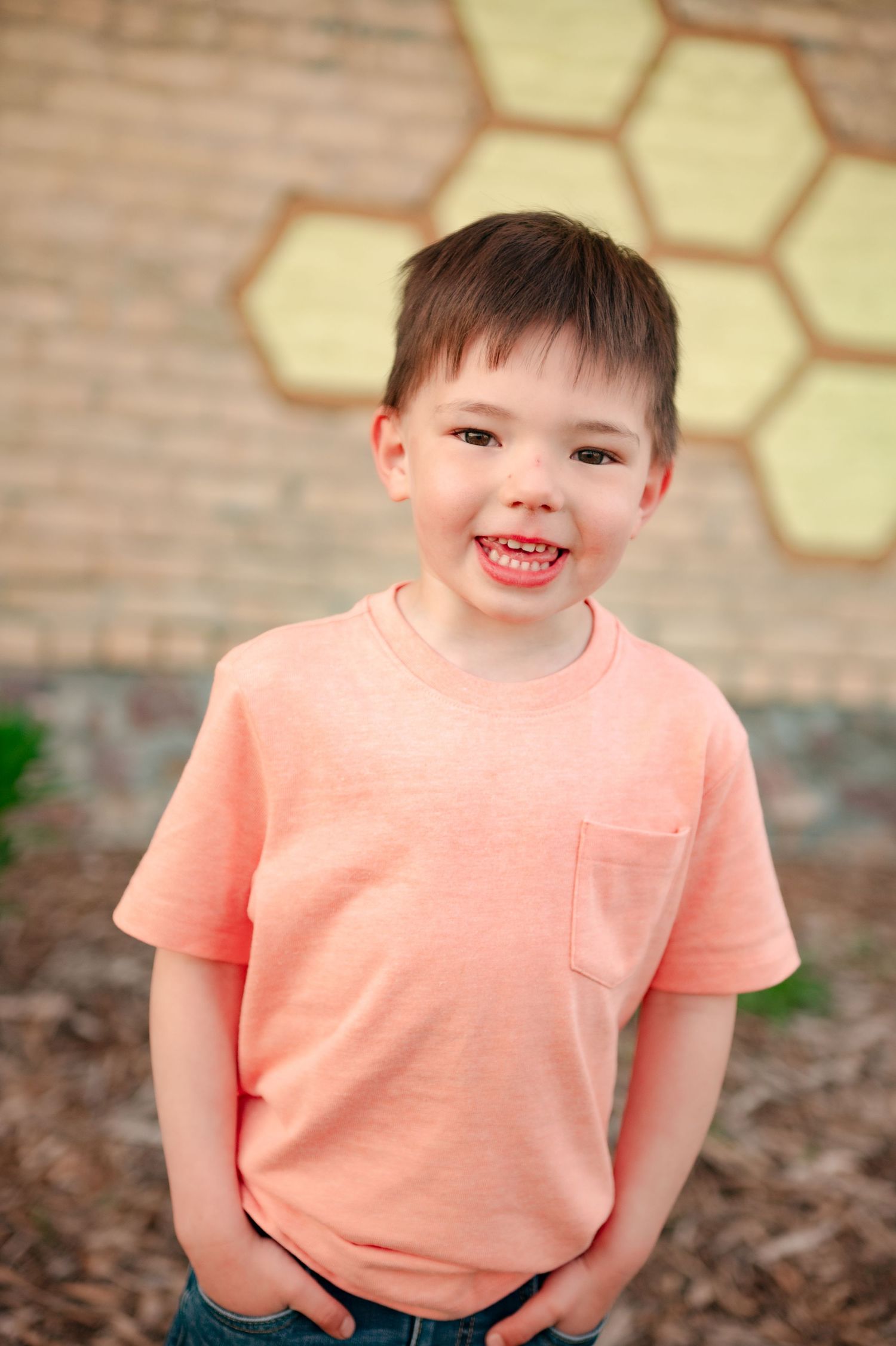 Cheerful portrait in coral t-shirt against brick wall with yellow honeycomb artwork.