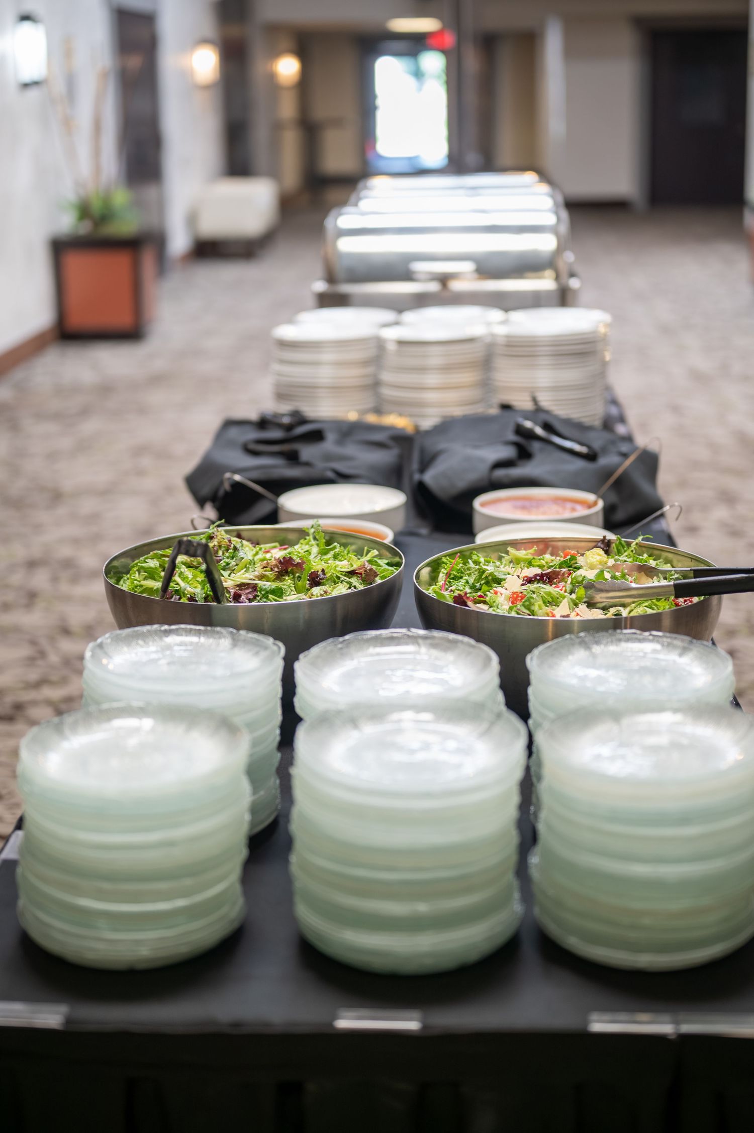 Catering display with salad bowls and serving containers arranged on a table in a hallway.
