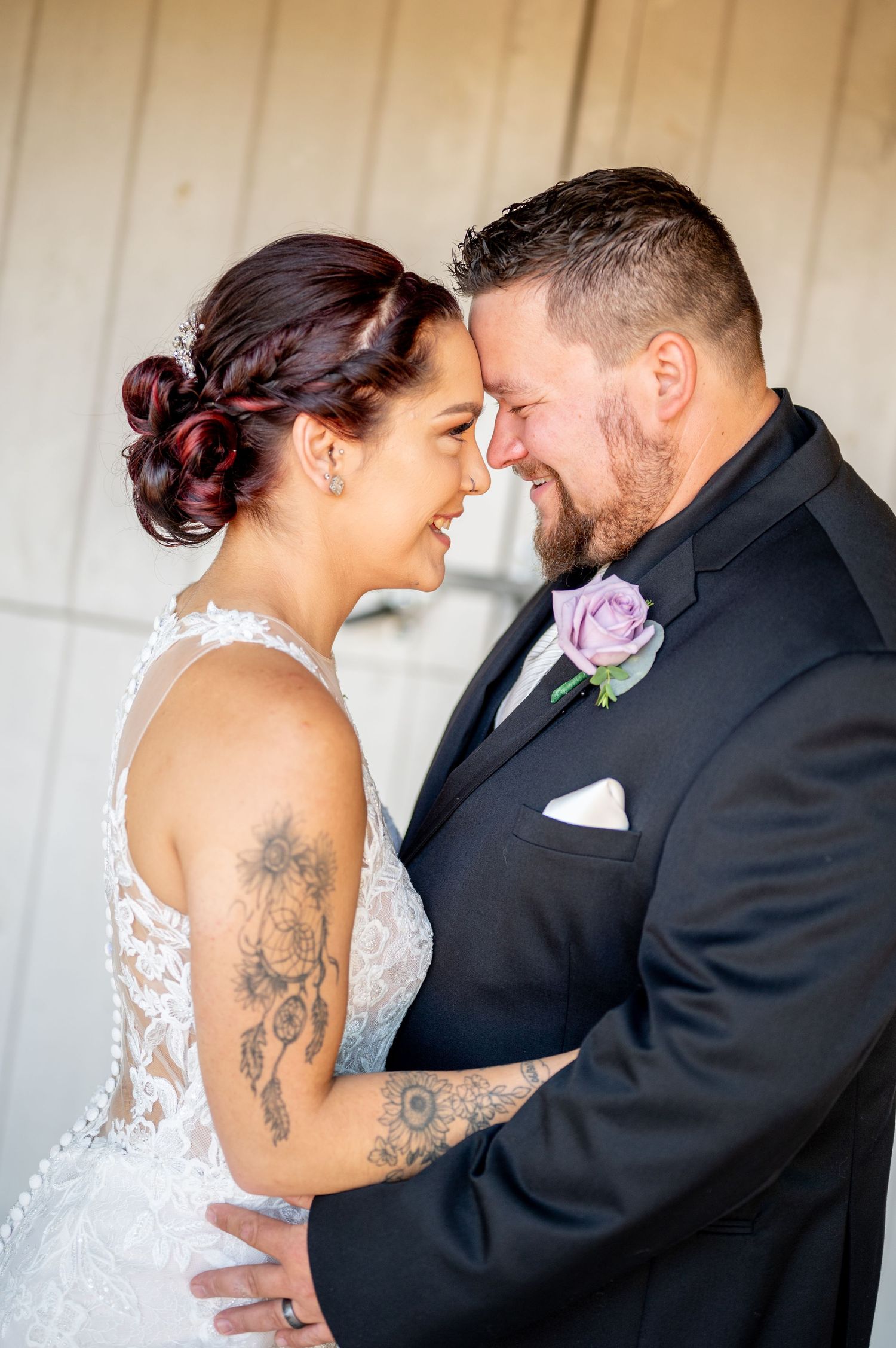 Close-up of bride with tattoos and groom sharing intimate moment in formal wedding attire.