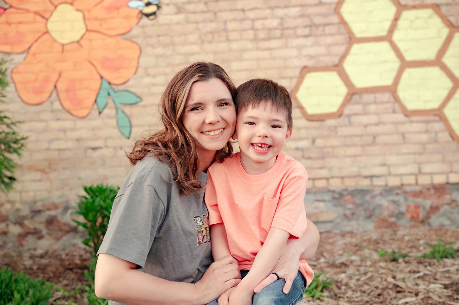 Natural smiles and laughter captured during outdoor family photo session with floral wall backdrop.