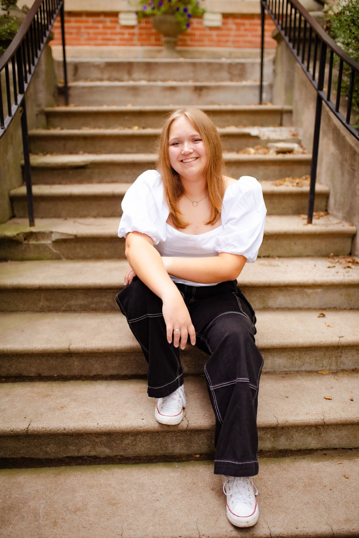 Person in white top and dark jeans sitting casually on concrete steps.