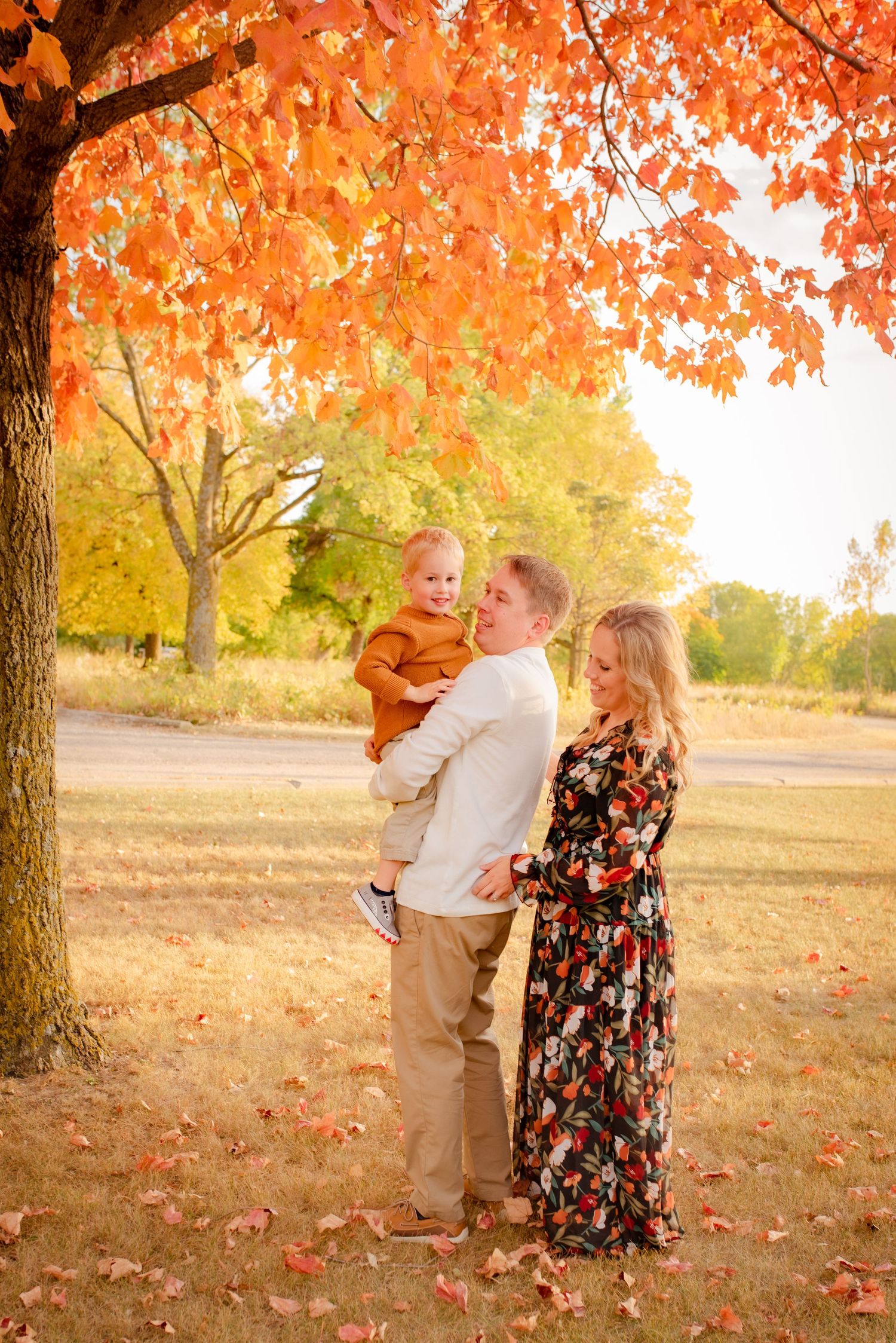 Family portrait under vibrant orange autumn tree with fallen leaves.