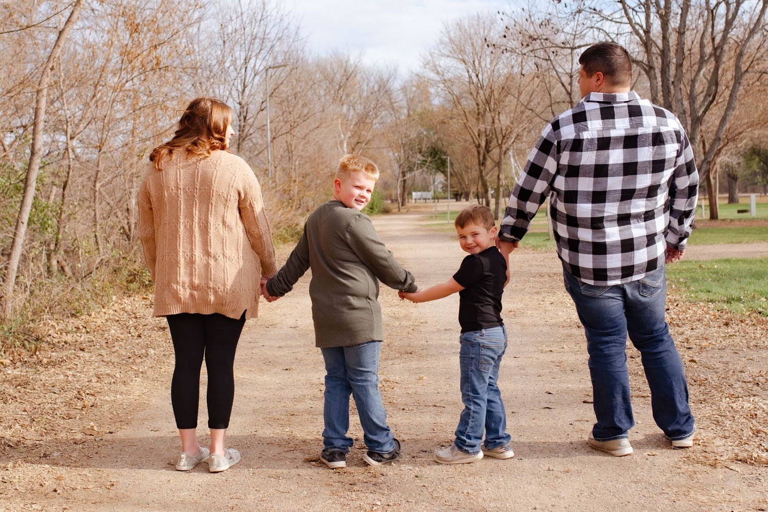 A family of four holding hands while walking together on a nature trail in autumn.