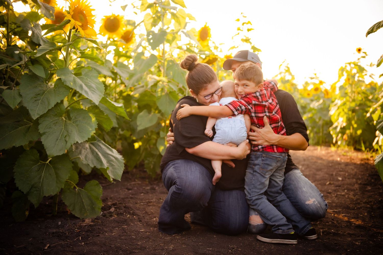 Family embracing in golden sunlight among tall sunflowers.