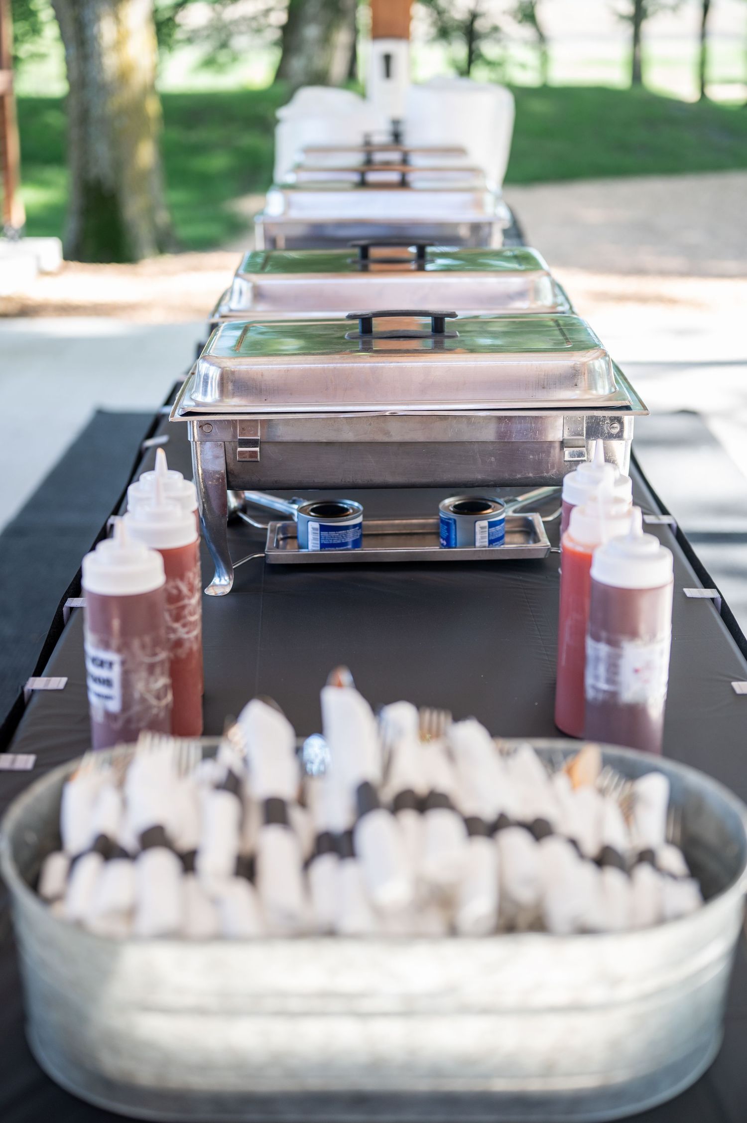 Catering setup with chafing dishes and beverage dispensers at an outdoor wedding reception.