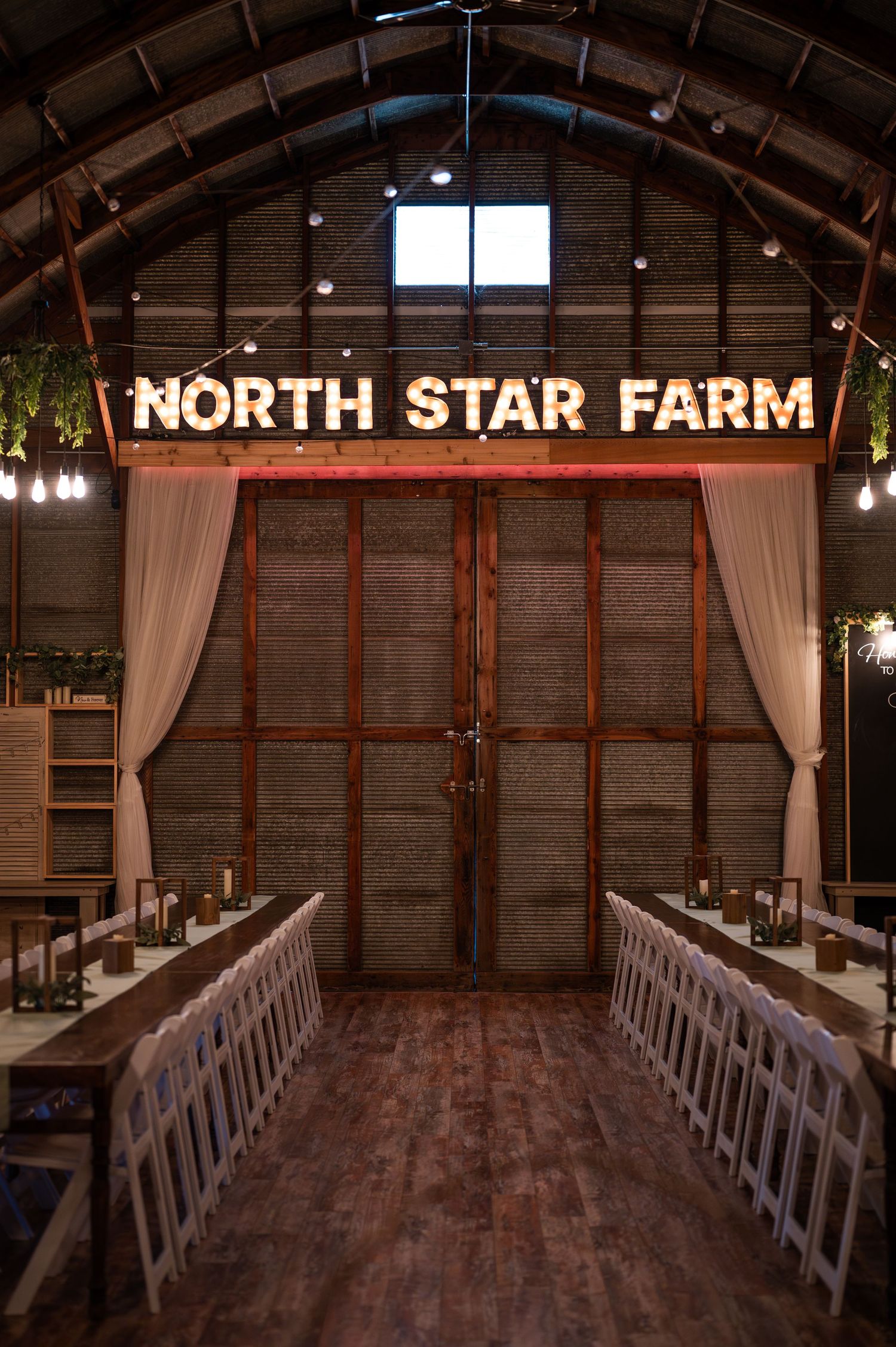 Rustic barn wedding venue interior at North Star Farm with illuminated signage and wooden benches.