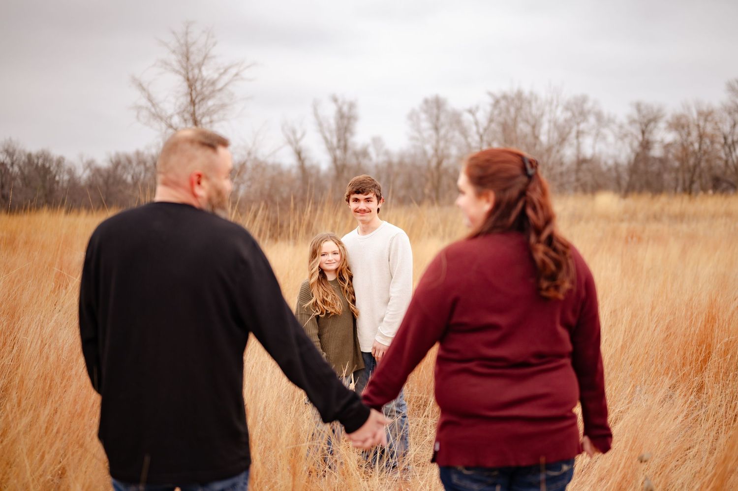 A family holds hands in a circle amid tall autumn grass during an outdoor photoshoot.