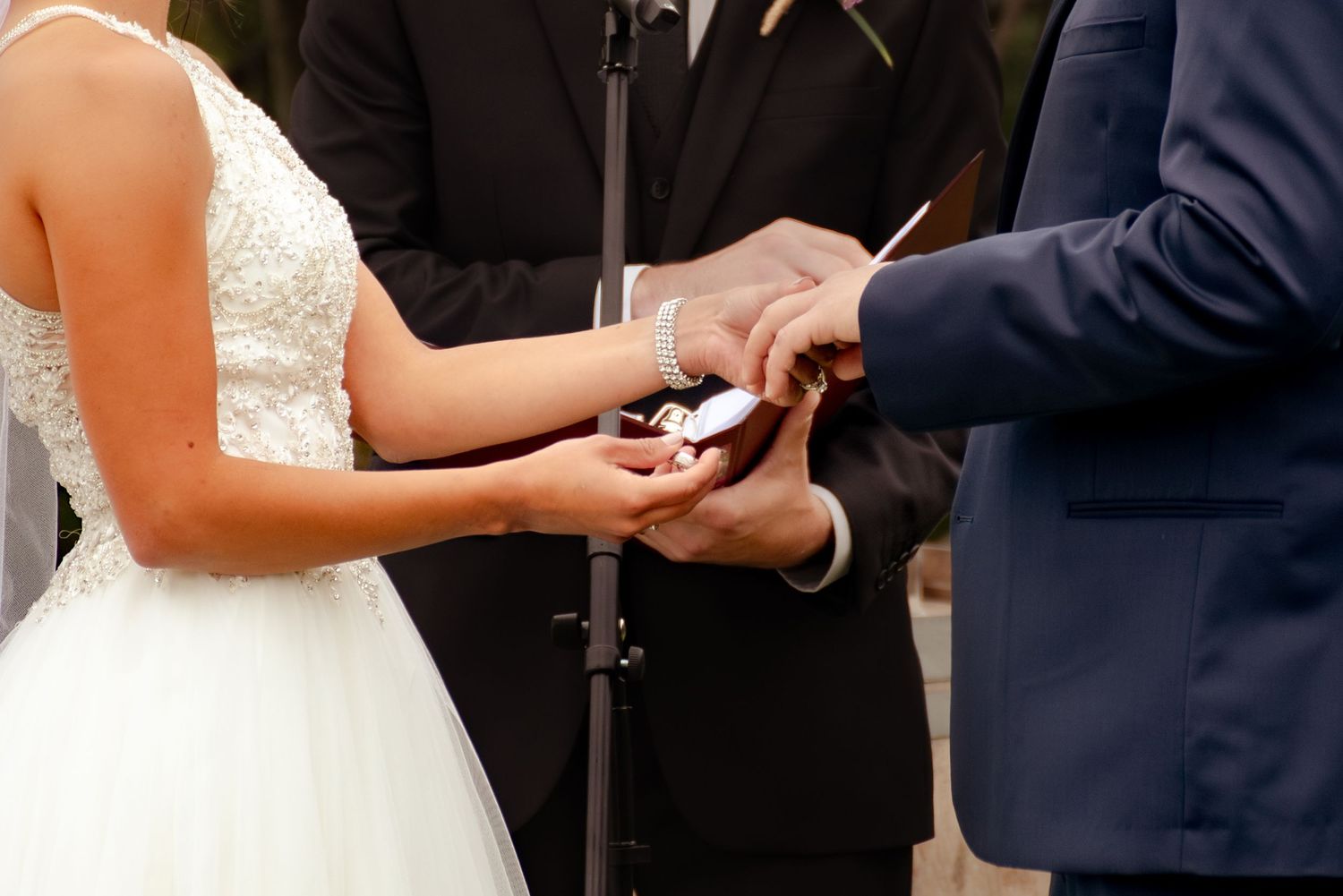 Close-up of hands exchanging wedding rings during an outdoor ceremony.