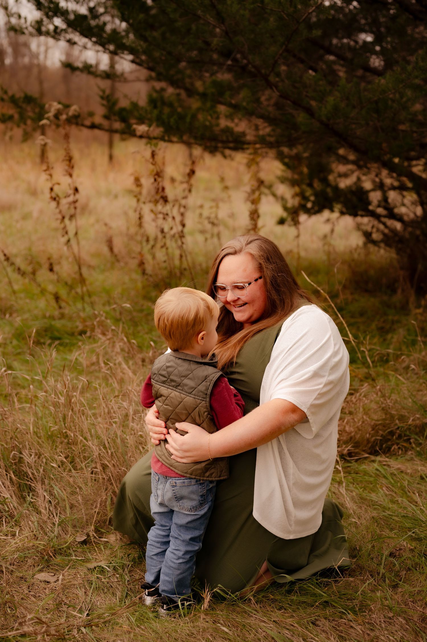 A tender family moment captured in a grassy field with warm autumn tones and natural lighting.