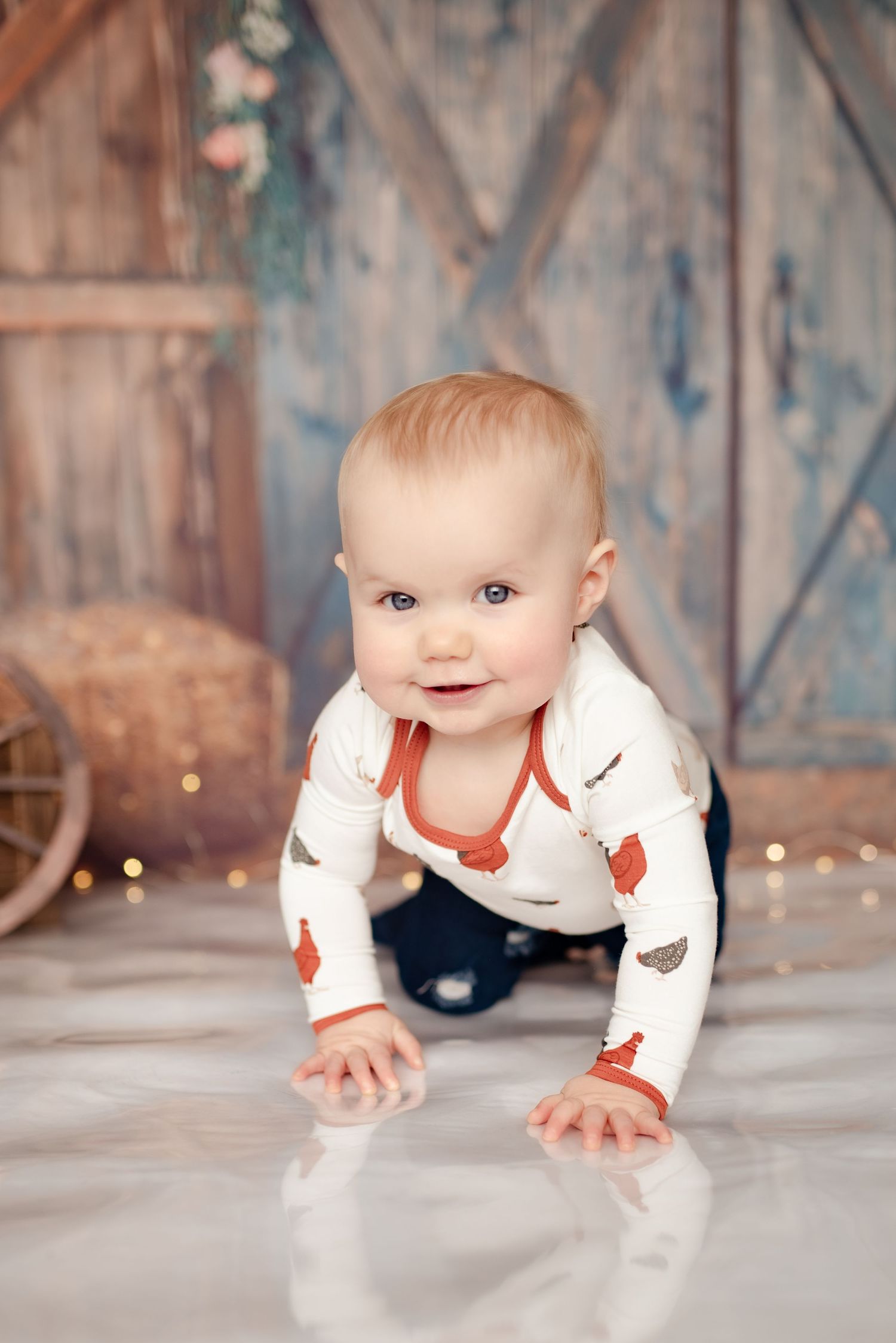 Crawling baby in heart print shirt on white floor with rustic barn door backdrop.