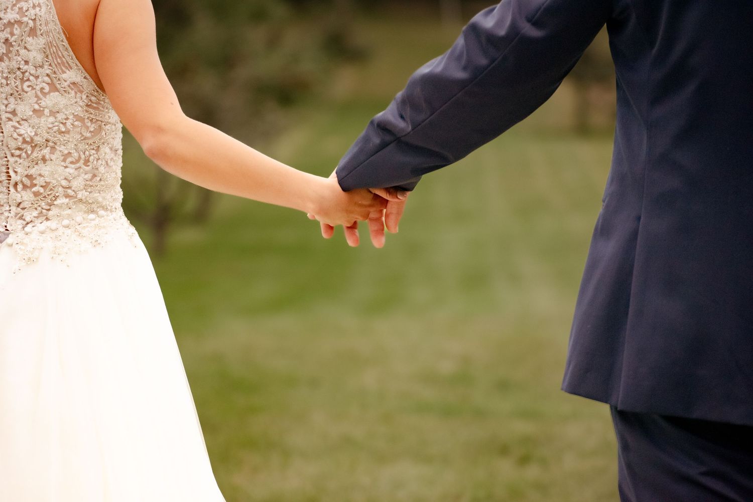 Close-up of newlyweds holding hands showing wedding rings against formal wedding attire.