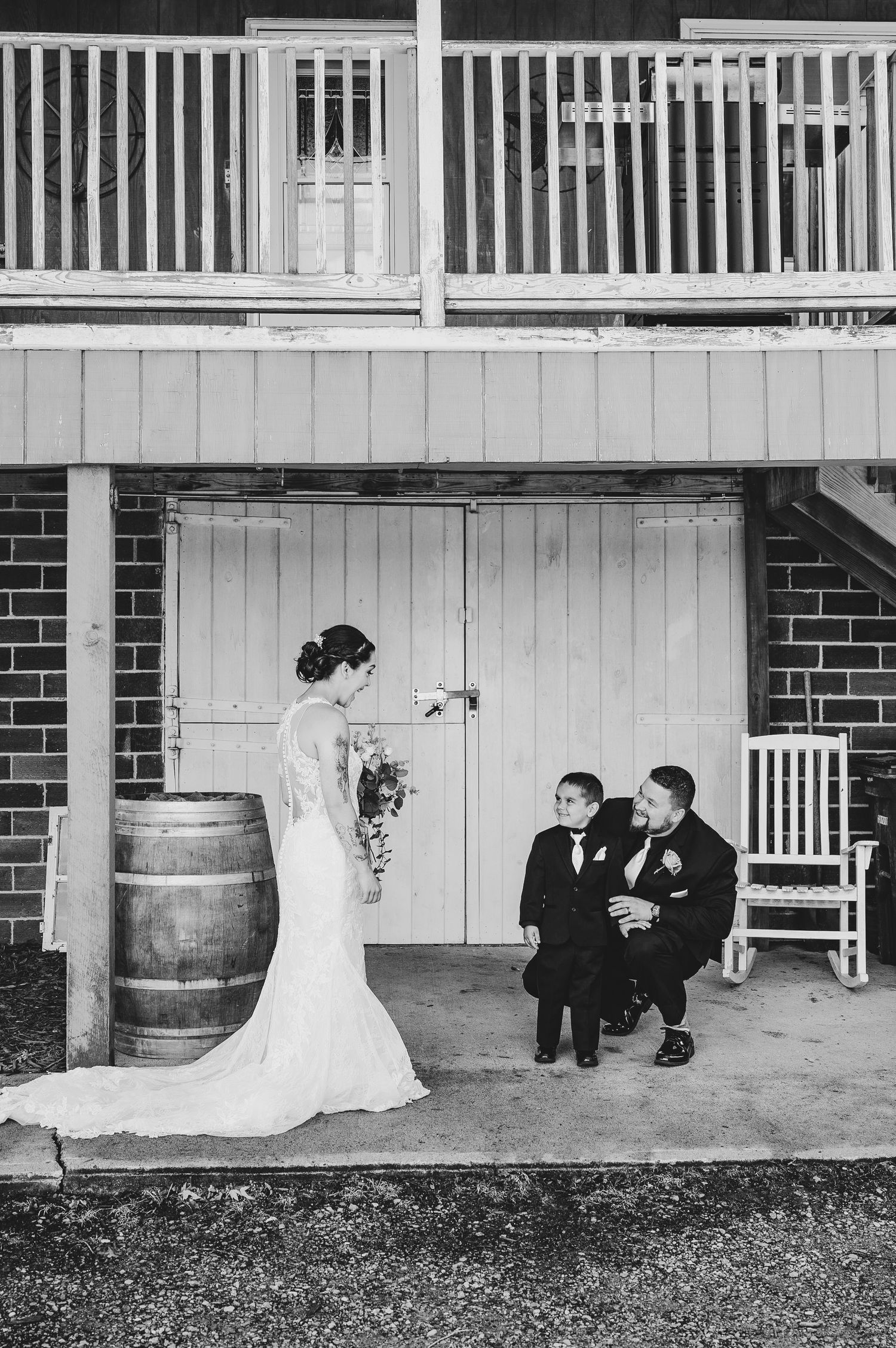 A black and white wedding photo featuring a bride in a mermaid dress with two children seated on a porch.