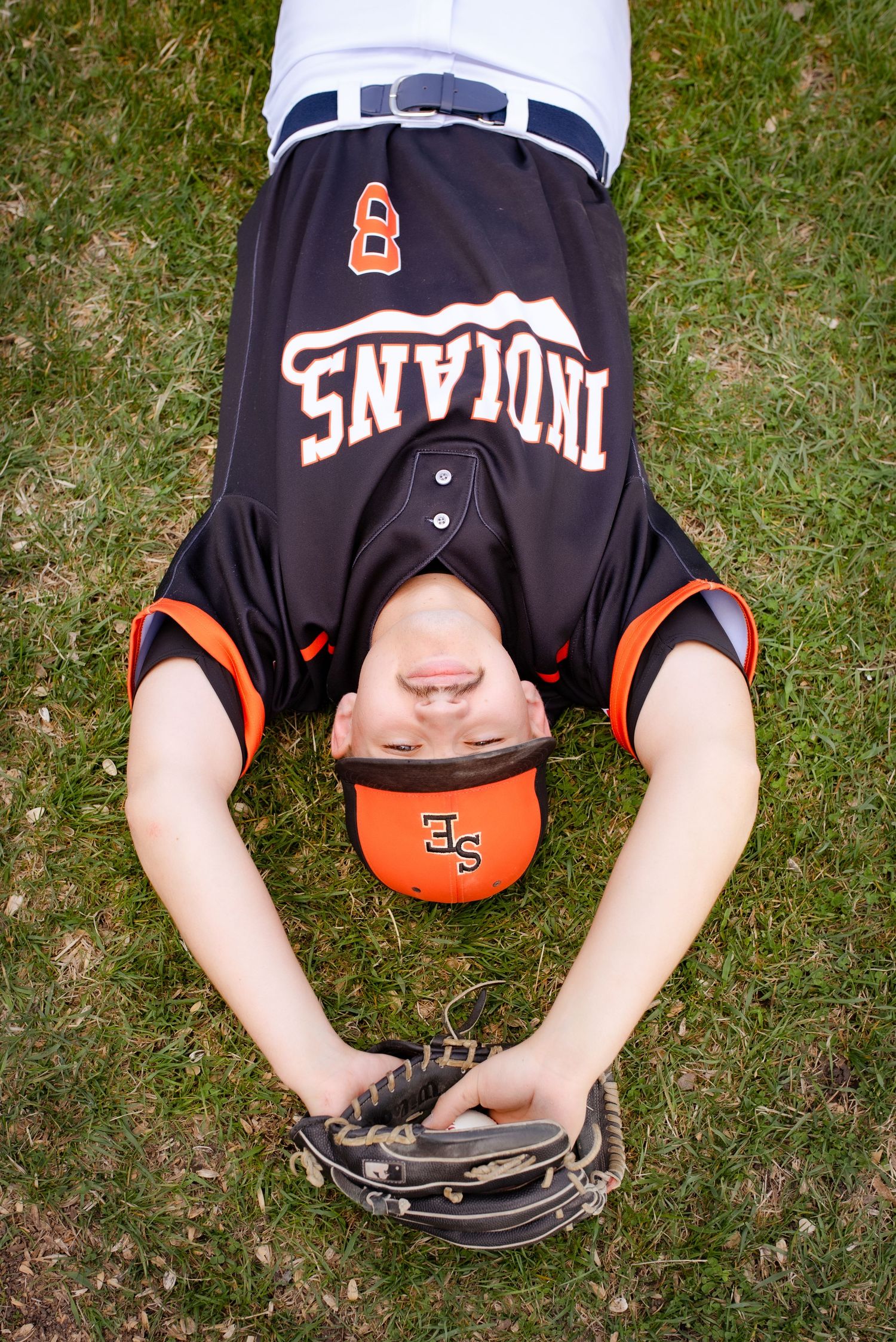 Baseball player lying on grass wearing Indians jersey with baseball glove and cap.