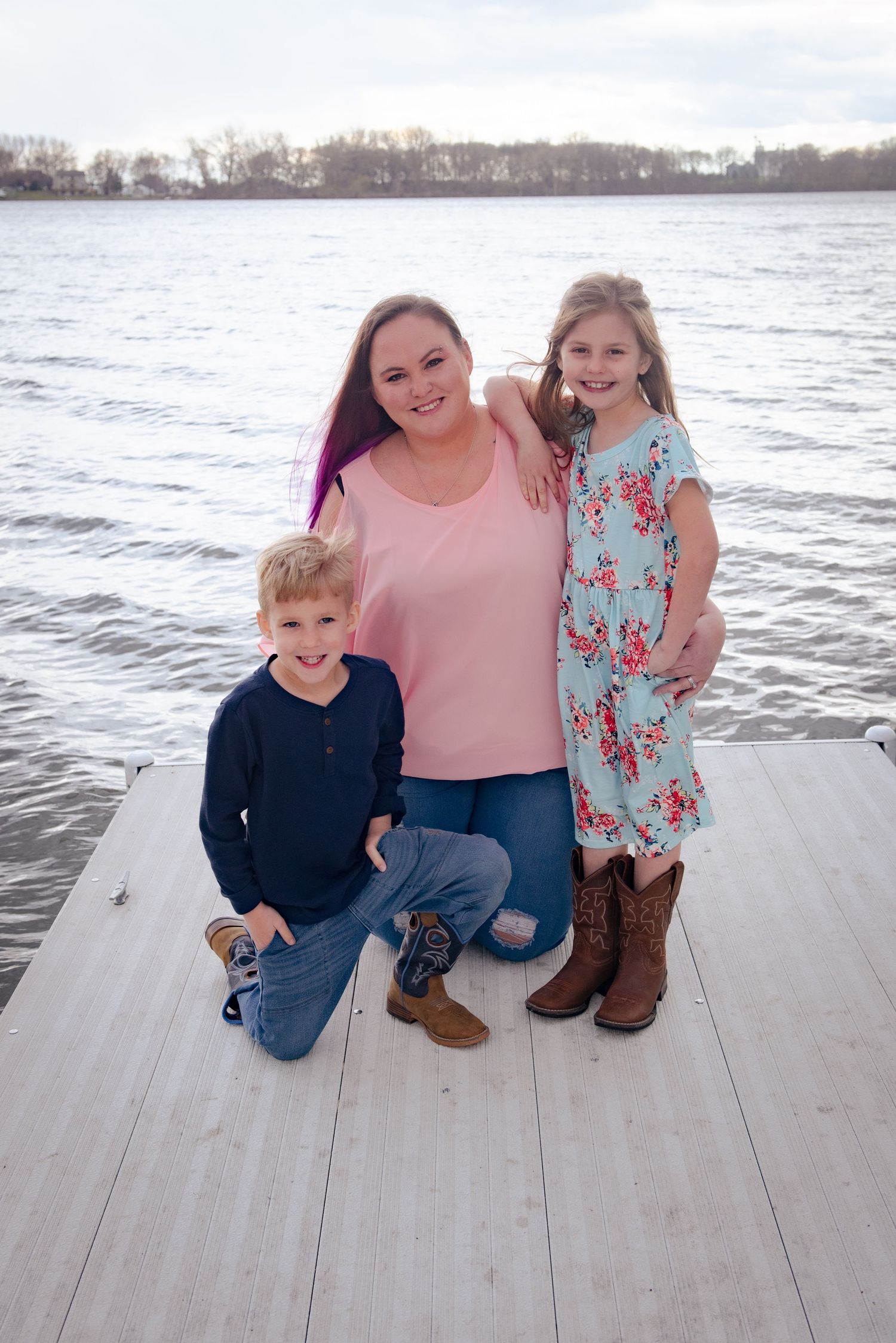 A family poses together on a wooden dock by a scenic lake during sunset.