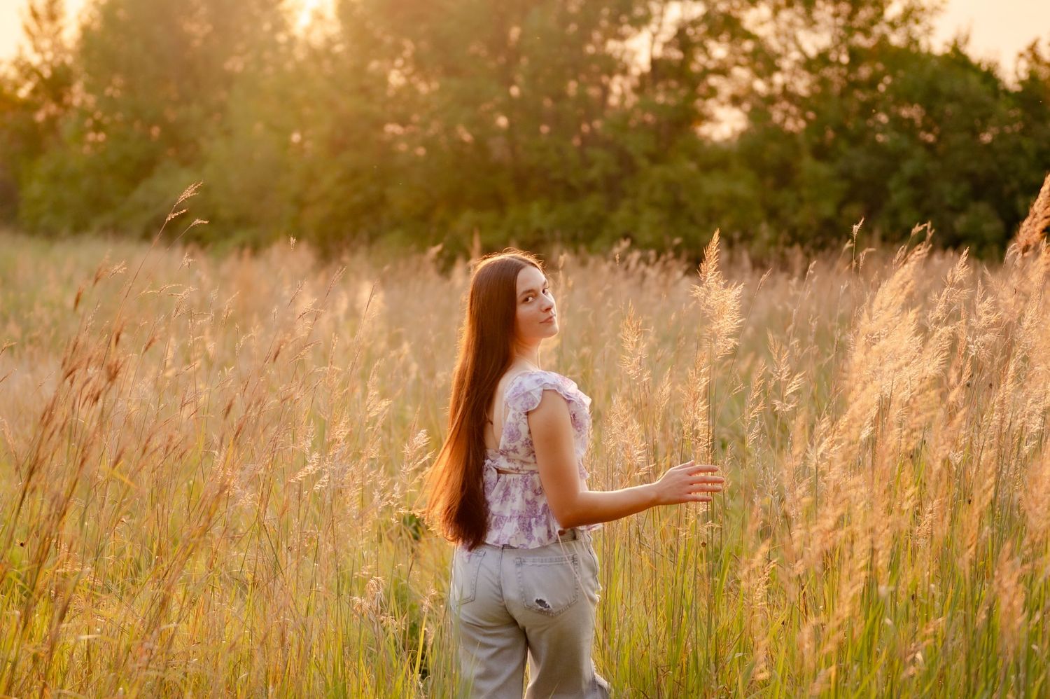 A golden sunset illuminates a field of tall grass as figures walk through the warm summer evening light.