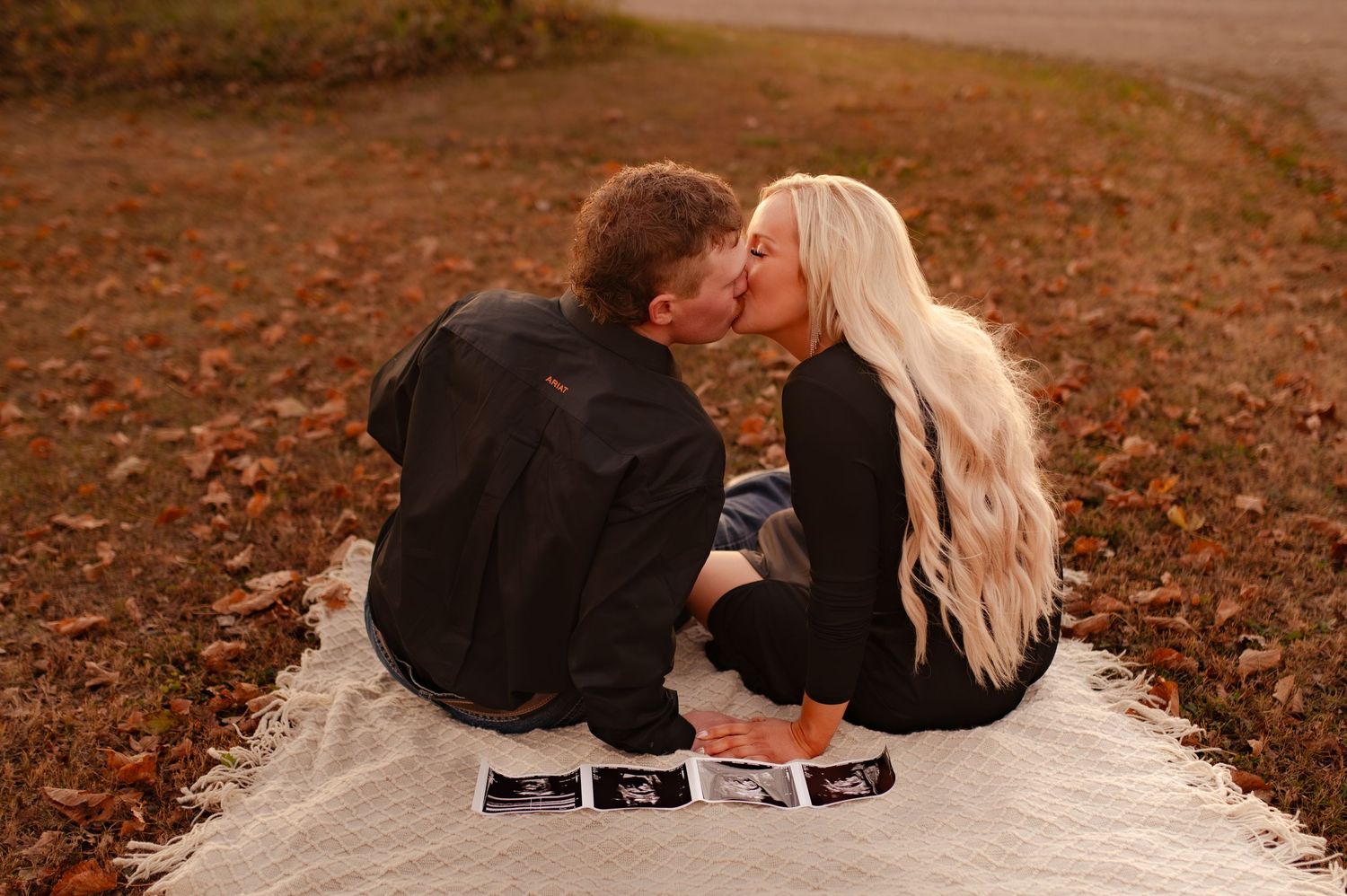 Couple lying on autumn ground looking at photos together during sunset.