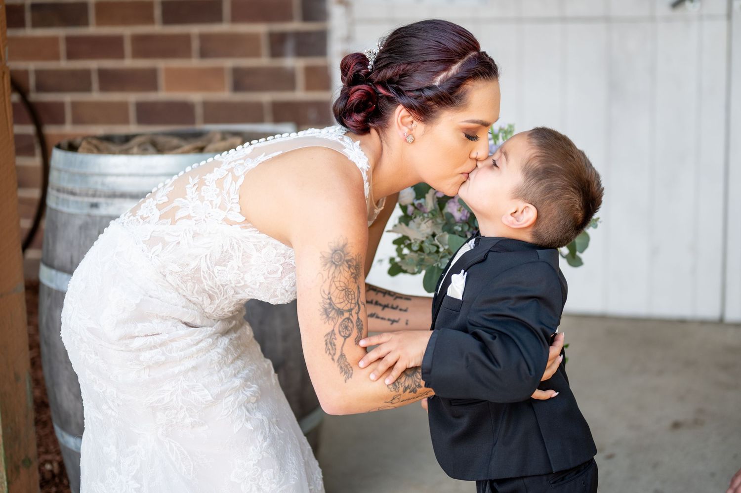 A touching wedding moment between a bride in a lace dress and a young ring bearer on a porch.
