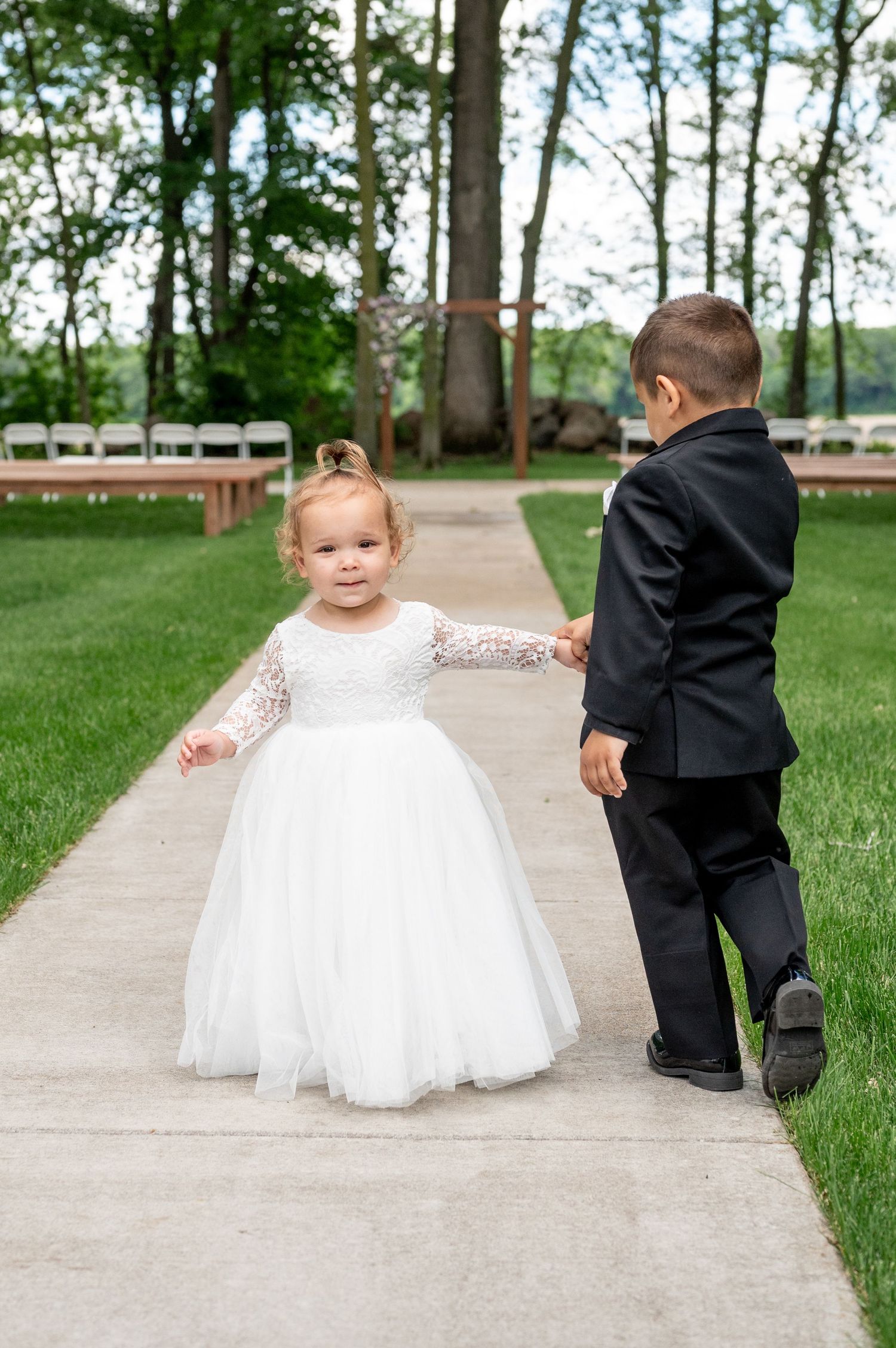 Two young children in formal attire walking on concrete path outdoors.