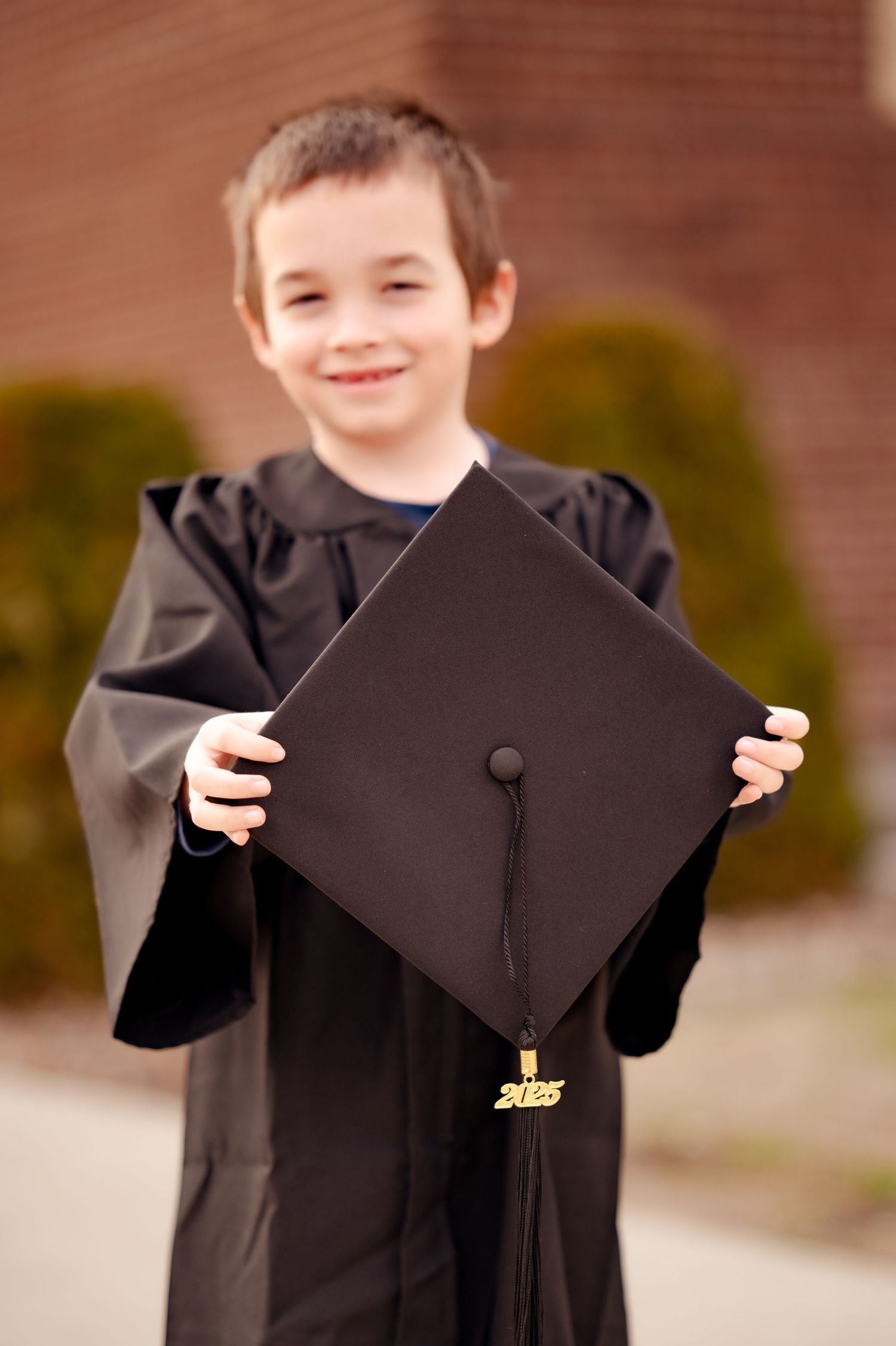 Graduate in black cap and gown proudly holding graduation cap with tassel outdoors.
