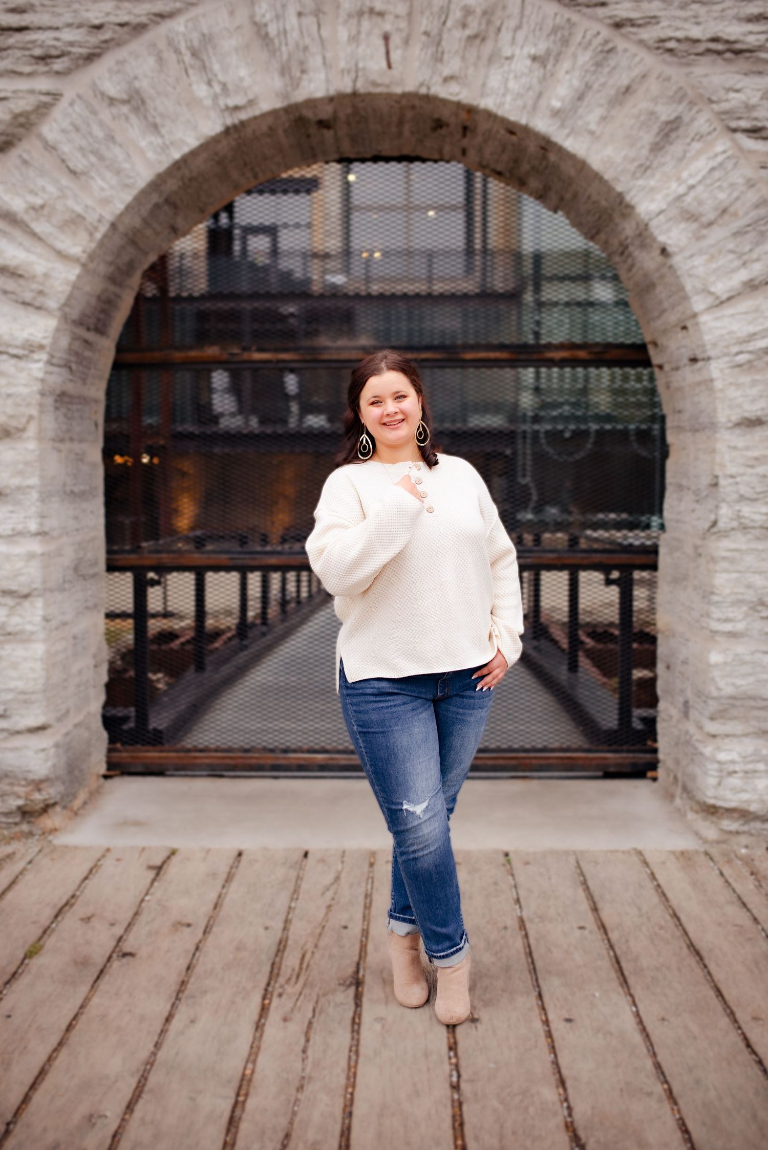 A person poses confidently under a stone archway on wooden planks.