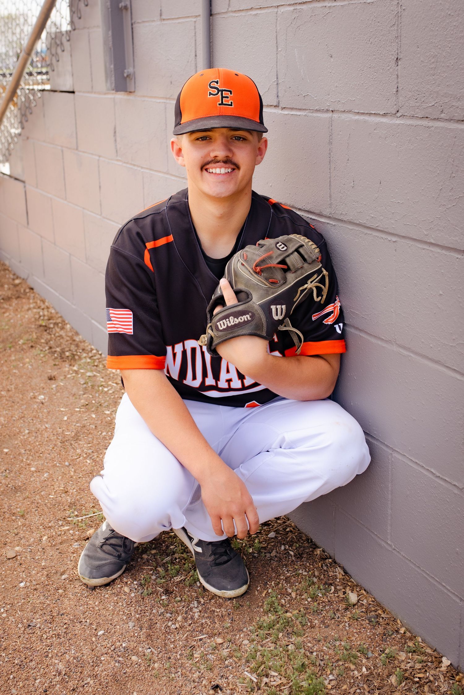 Baseball player in Indians uniform crouches by wall holding baseball glove.
