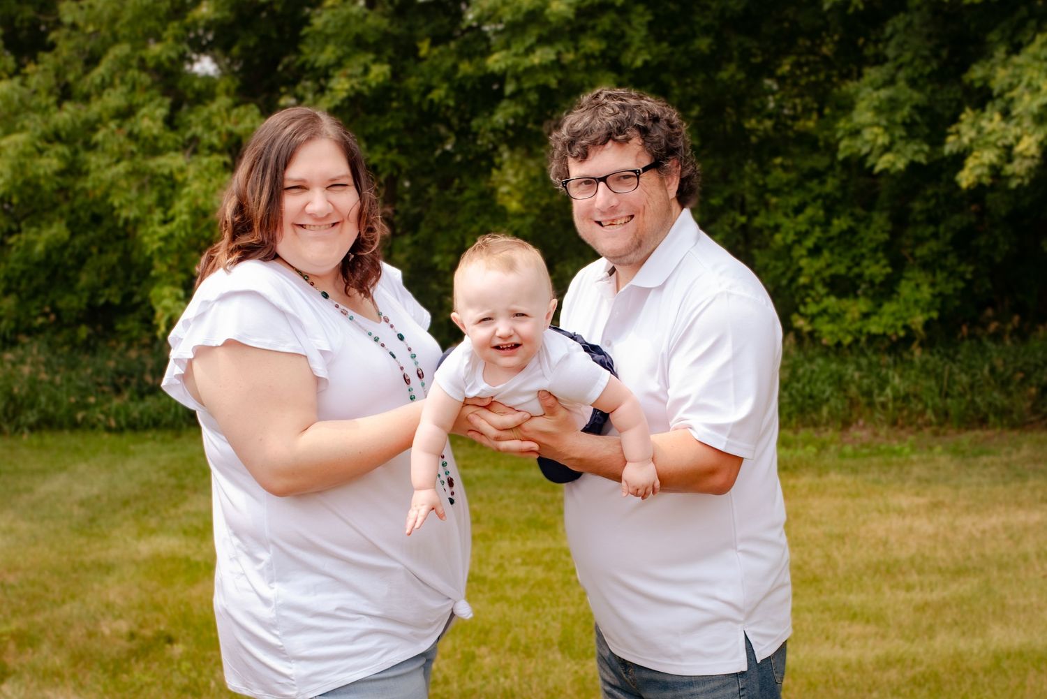 Happy family shares joyful moment with their baby in outdoor summer setting.
