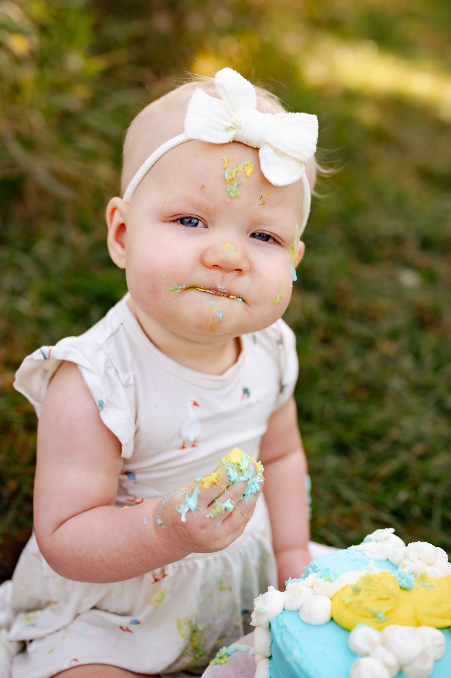 Baby with frosting-covered face during outdoor cake smash photo session.