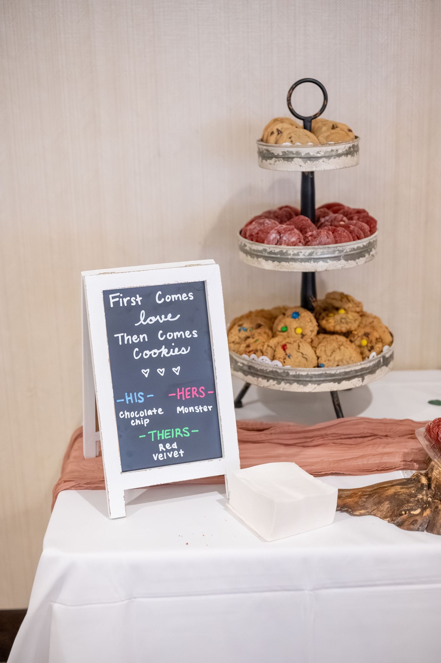 Three-tiered cookie display stand with chalkboard sign reading 'First Comes Love Then Comes Cookies'.
