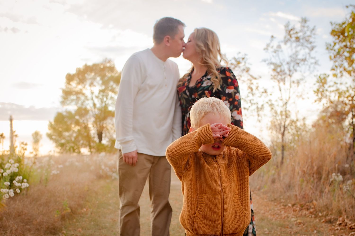 Family shares tender moment during golden hour photoshoot as child covers face playfully.
