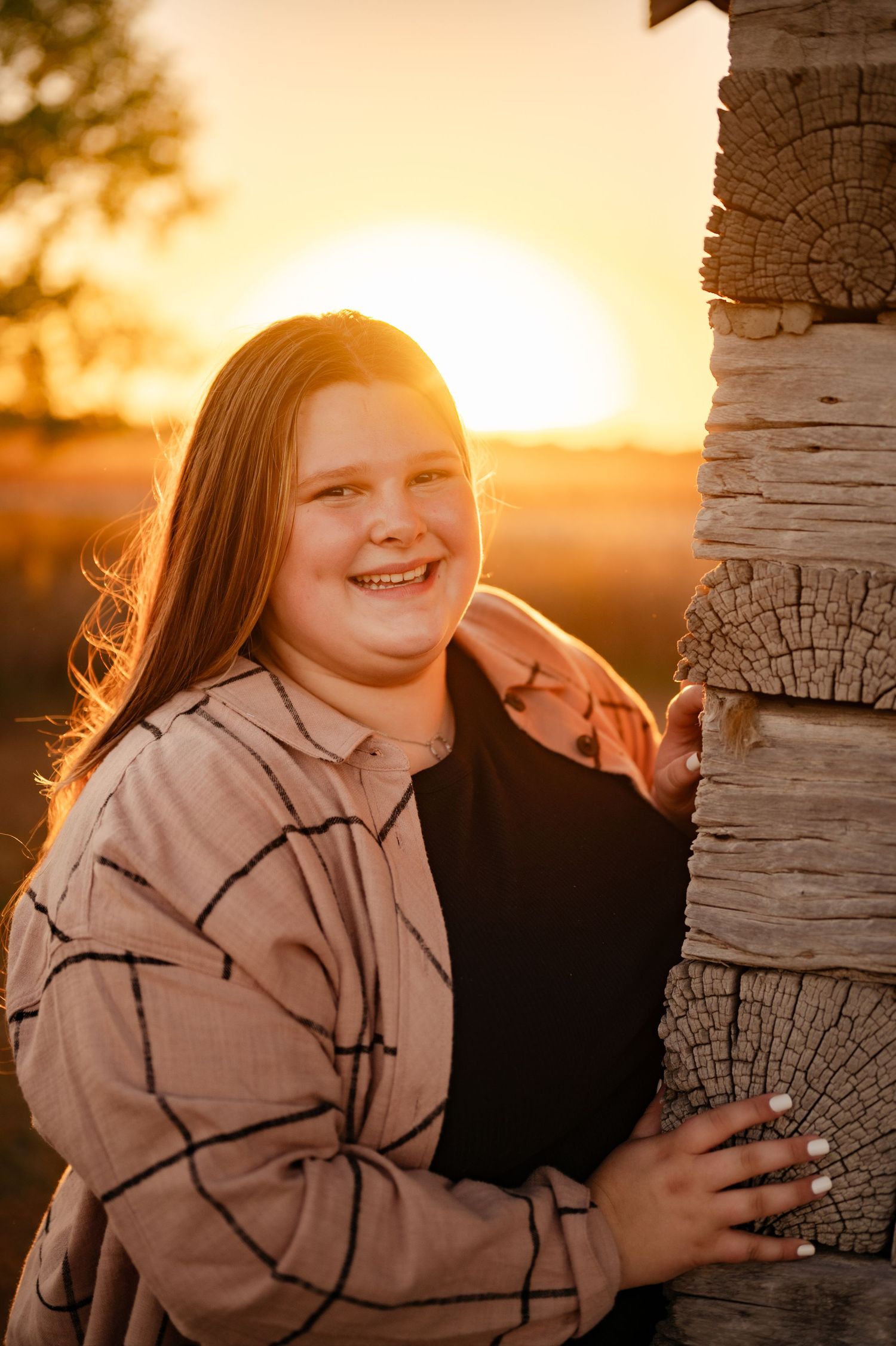 A joyful sunset portrait against rustic wooden logs with golden hour lighting.