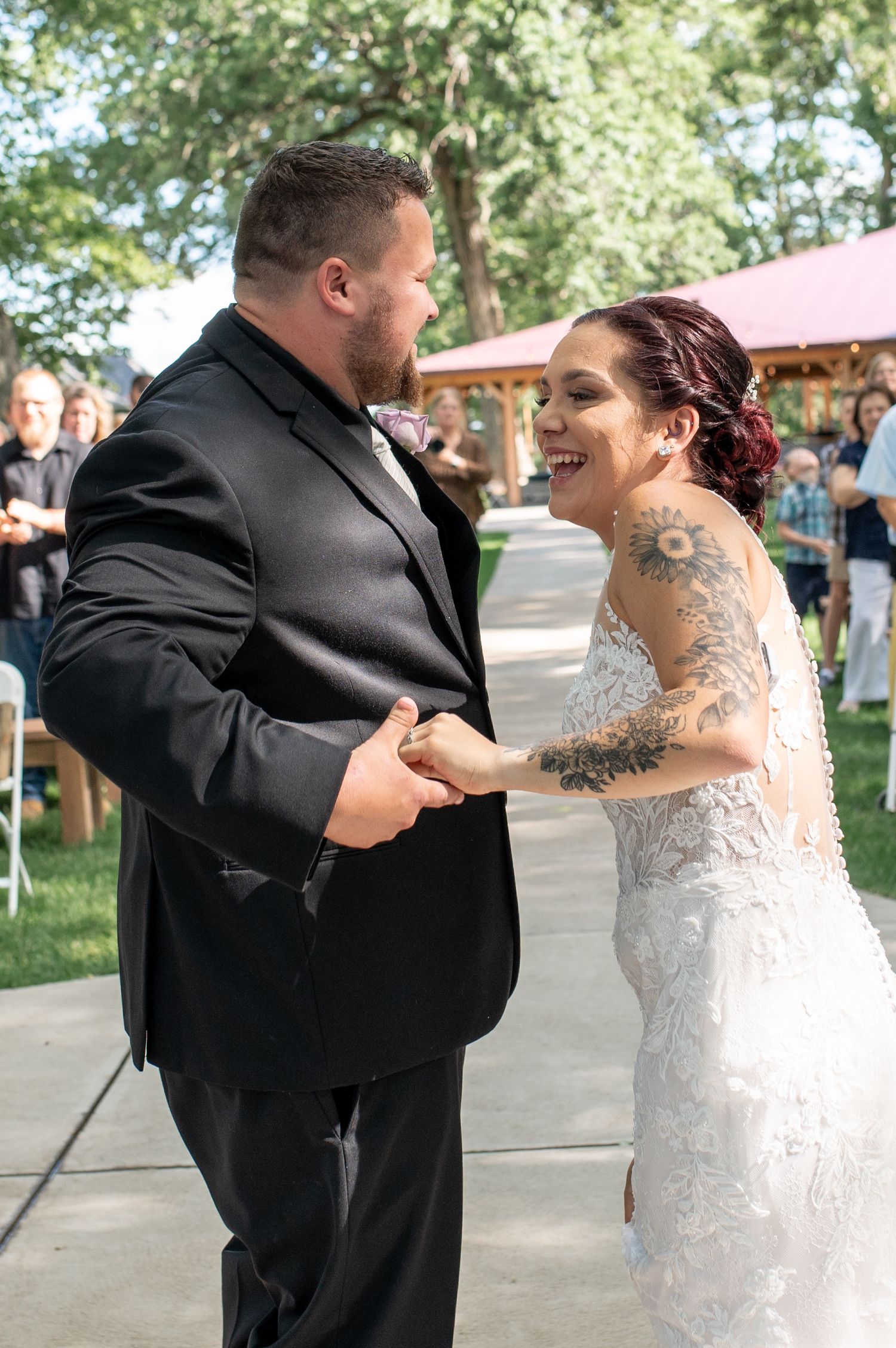 A couple shares a joyful moment during their first dance at an outdoor wedding reception.