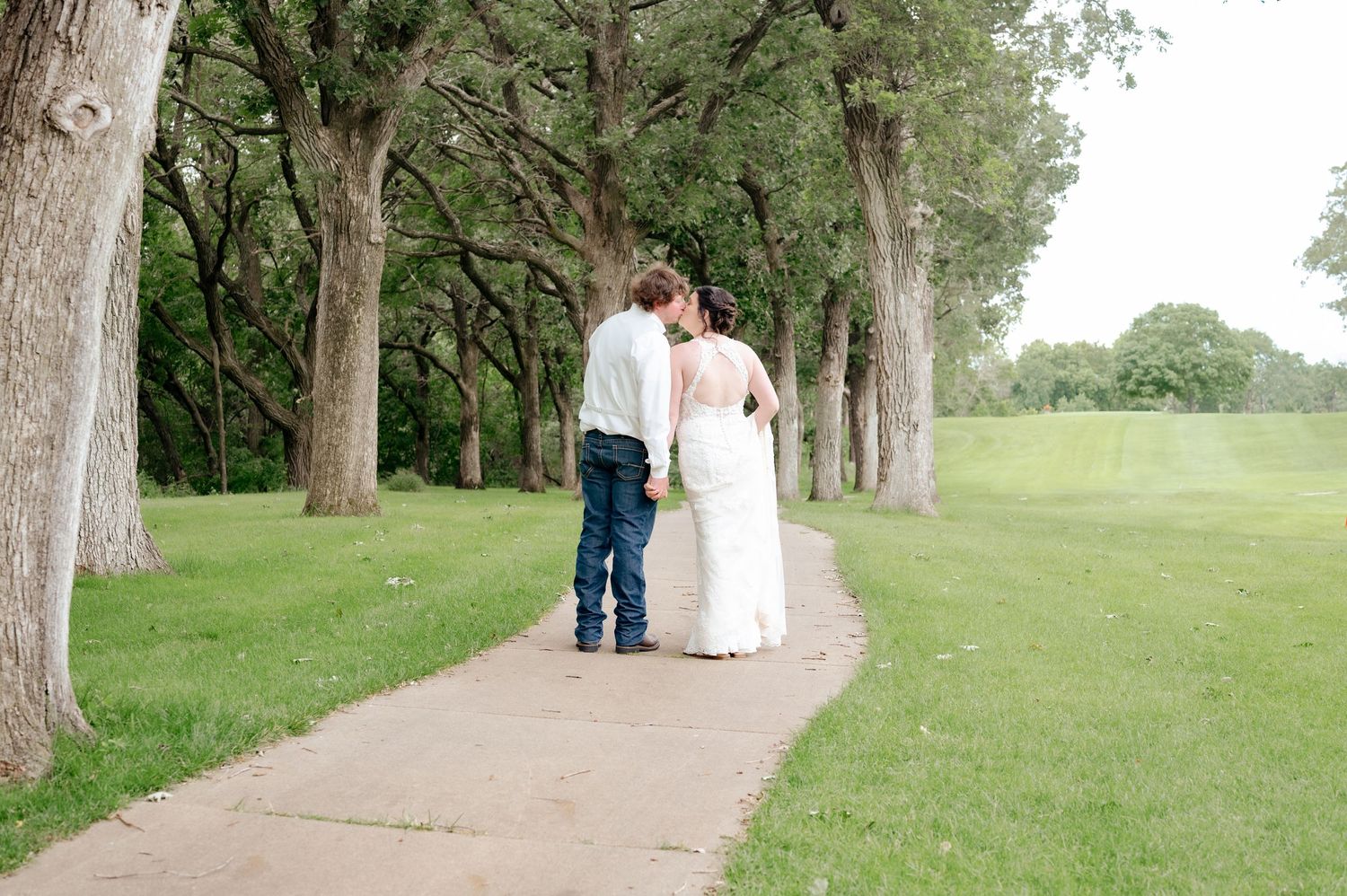 Couple walking down tree-lined path during wedding celebration.