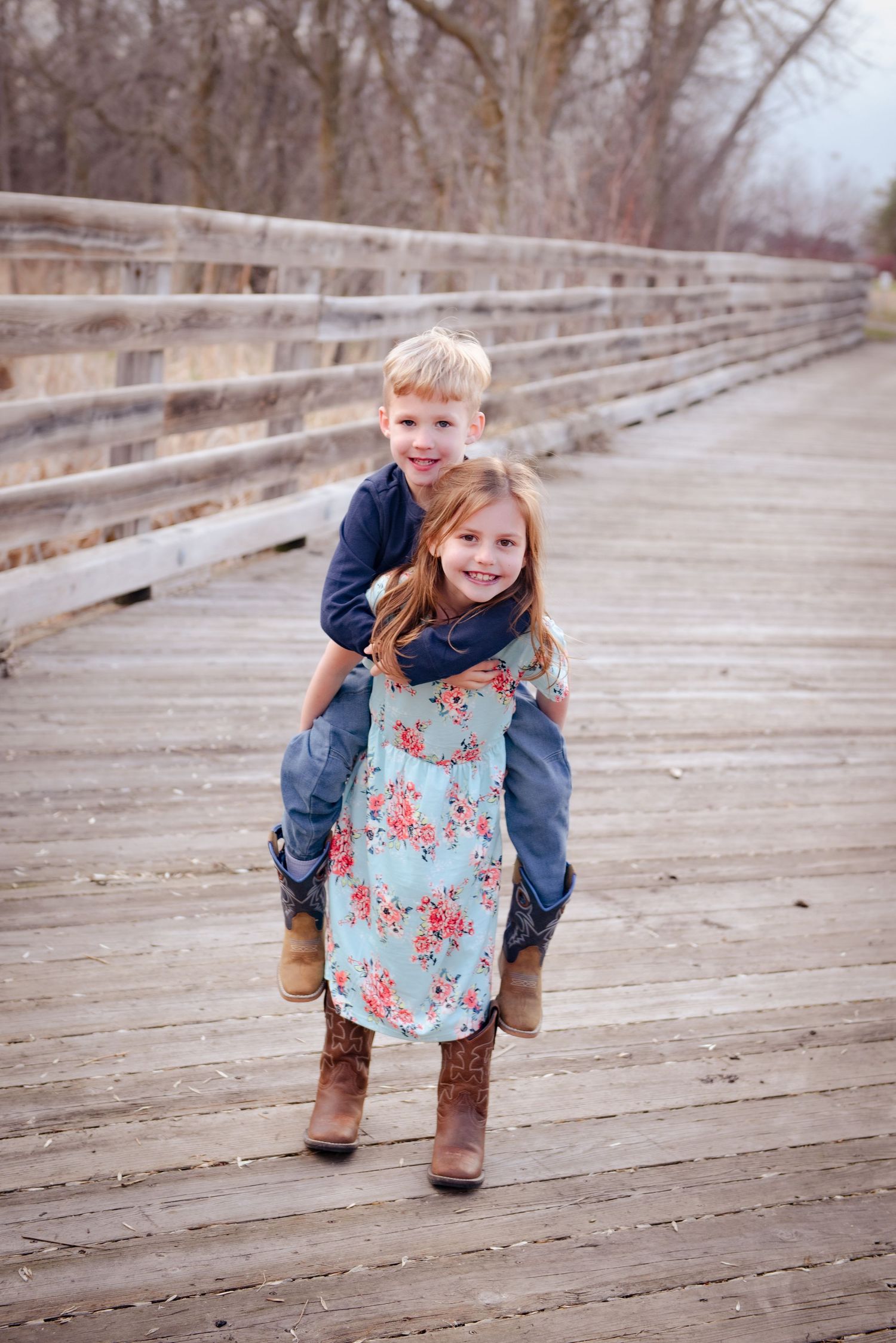 Two children playing and having fun on a wooden boardwalk with one giving the other a piggyback ride.