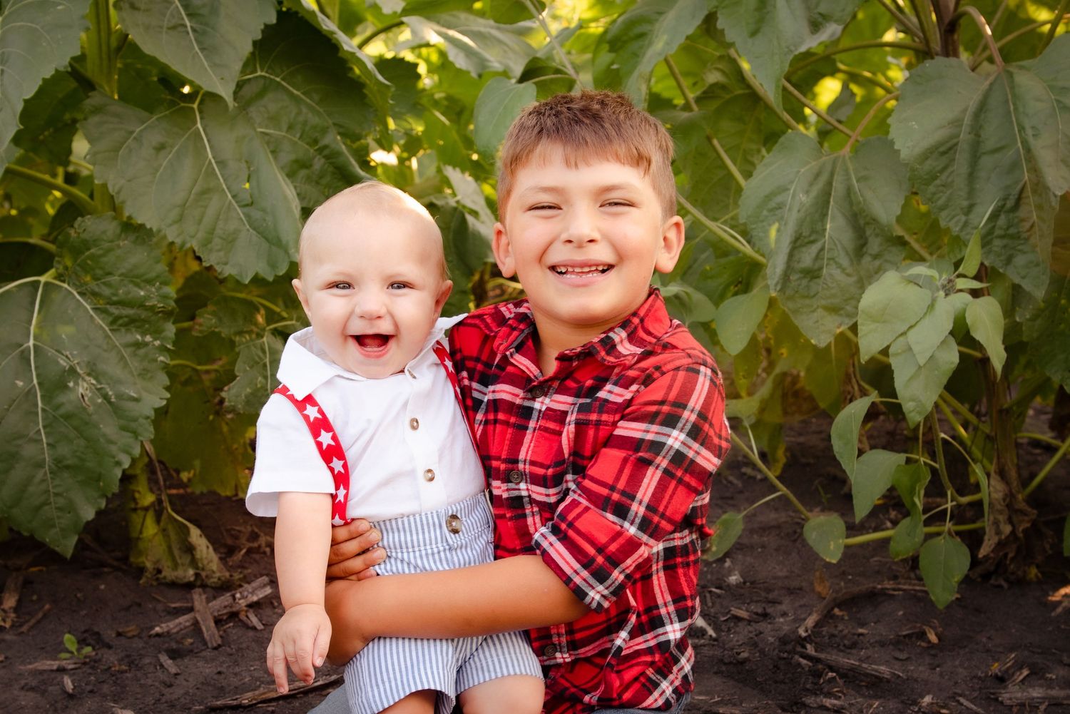 Two cheerful children sharing a sweet moment together in front of lush green leaves in a garden setting.