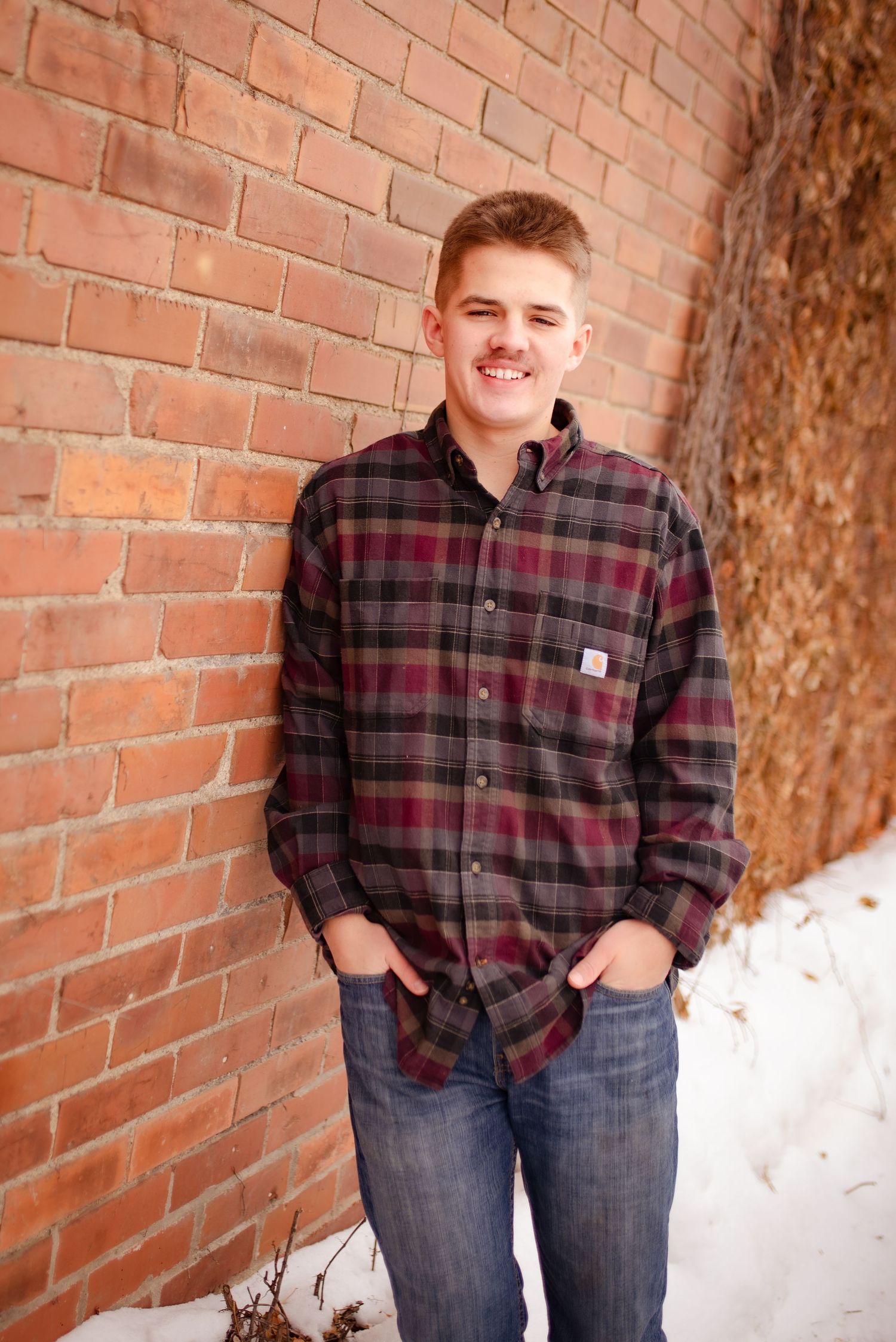 Portrait against brick wall wearing plaid flannel shirt and jeans in natural lighting.