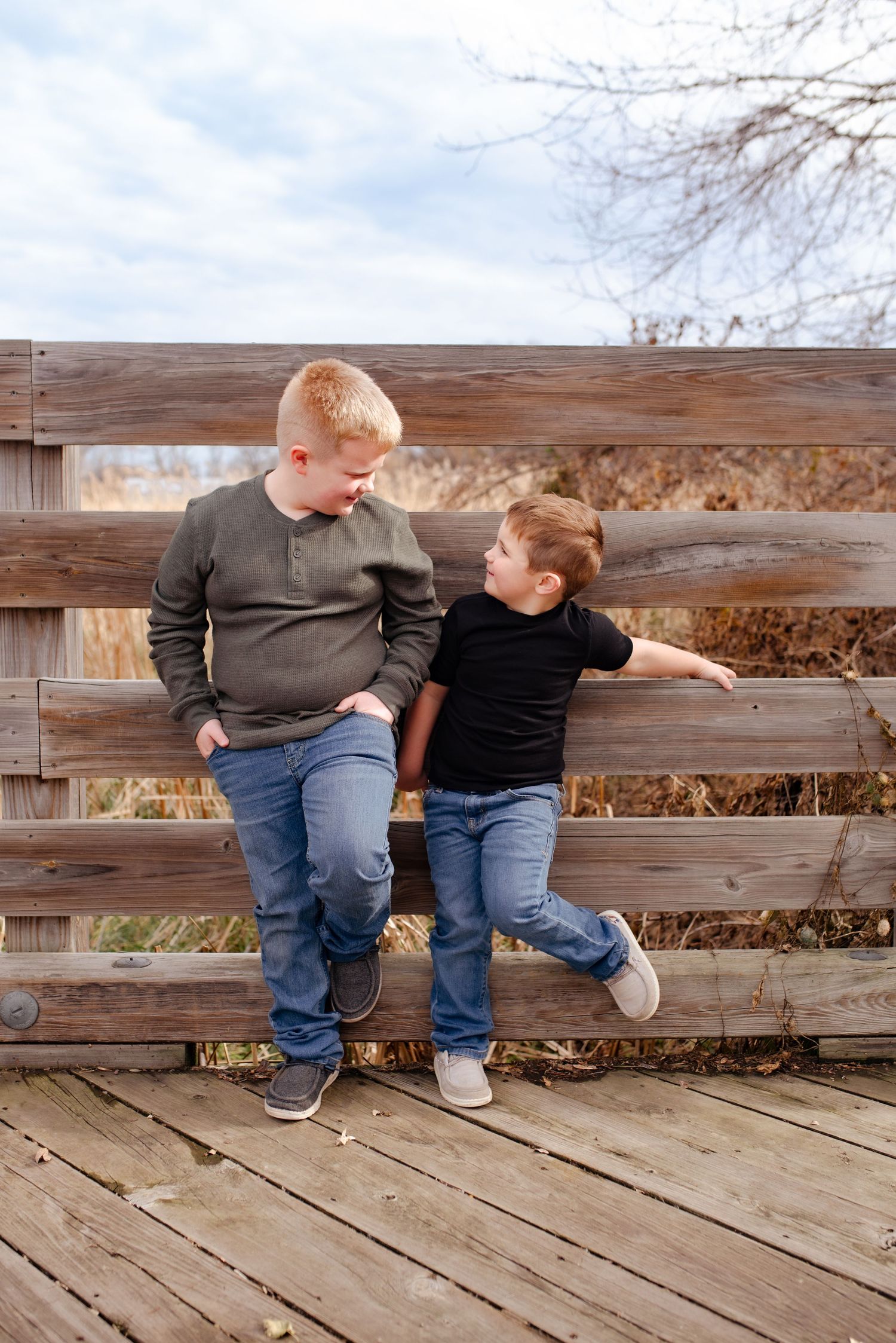 Two children relaxing on wooden bridge railing during outdoor photo session.