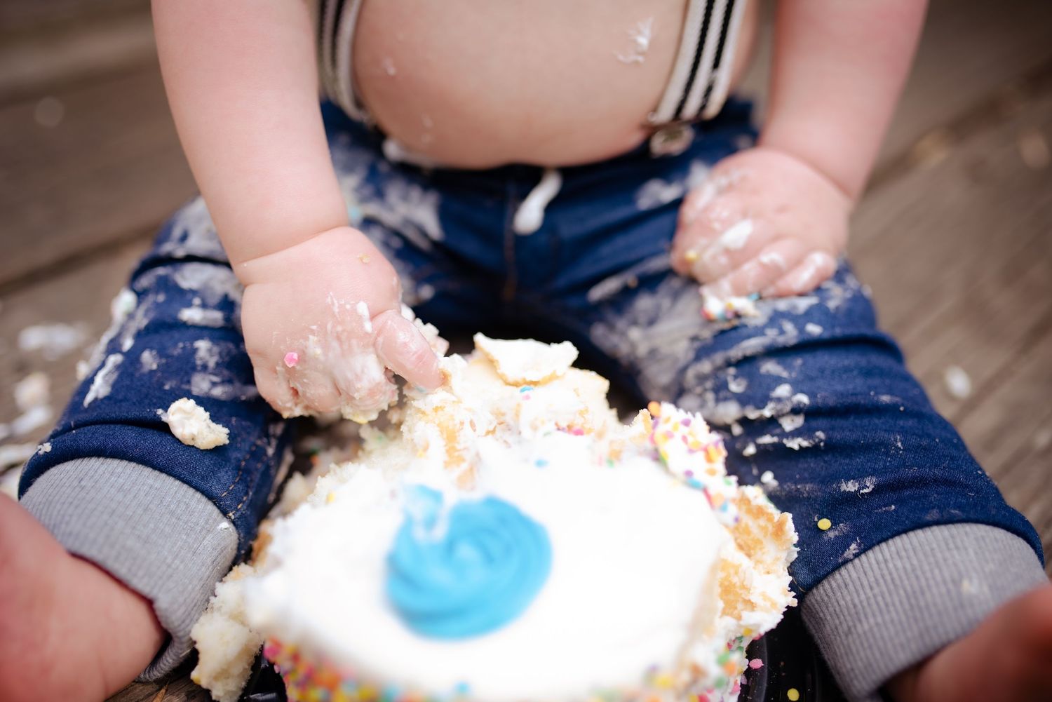 Close-up of tiny hands and legs covered in cake frosting during a cake smash photoshoot.