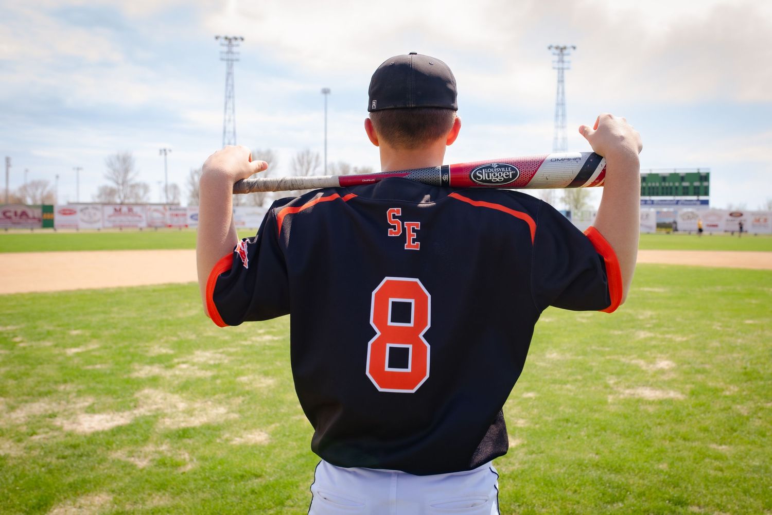 Baseball player wearing black jersey with number 8 stands ready at bat on field with stadium lights in background.